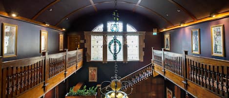 A grand interior with a high arched ceiling, wooden railings, and a central staircase.