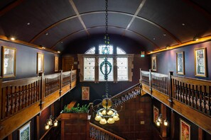 A grand interior with a high arched ceiling, wooden railings, and a central staircase.