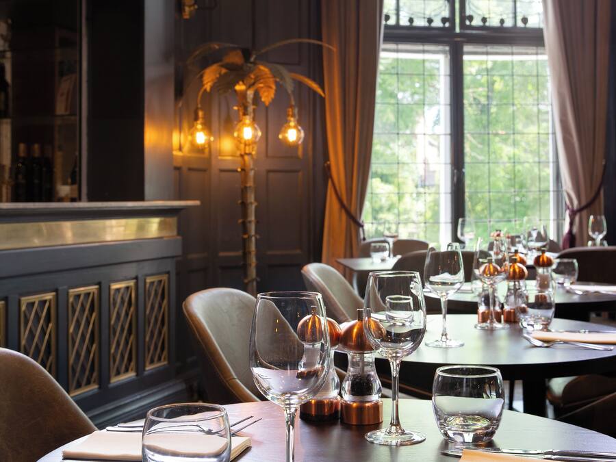 A dining area with tables set for a meal, a bar area with bottles, and a large window with curtains.