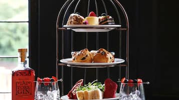 A three-tiered dessert stand with various pastries and fruits, a bottle of York Gin, and two glasses with fruit garnishes on a table.