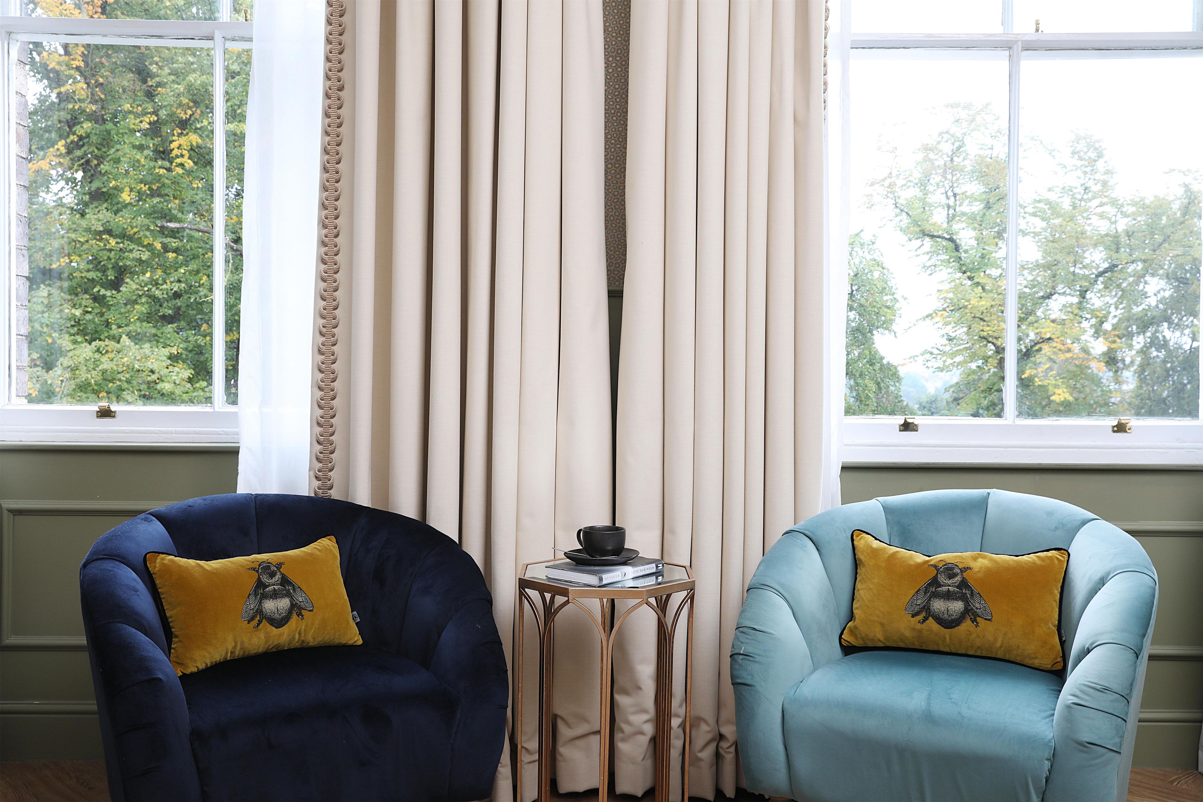 A room with two armchairs, a small table with a cup and books, and a window with curtains.