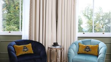 A room with two armchairs, a small table with a cup and books, and a window with curtains.