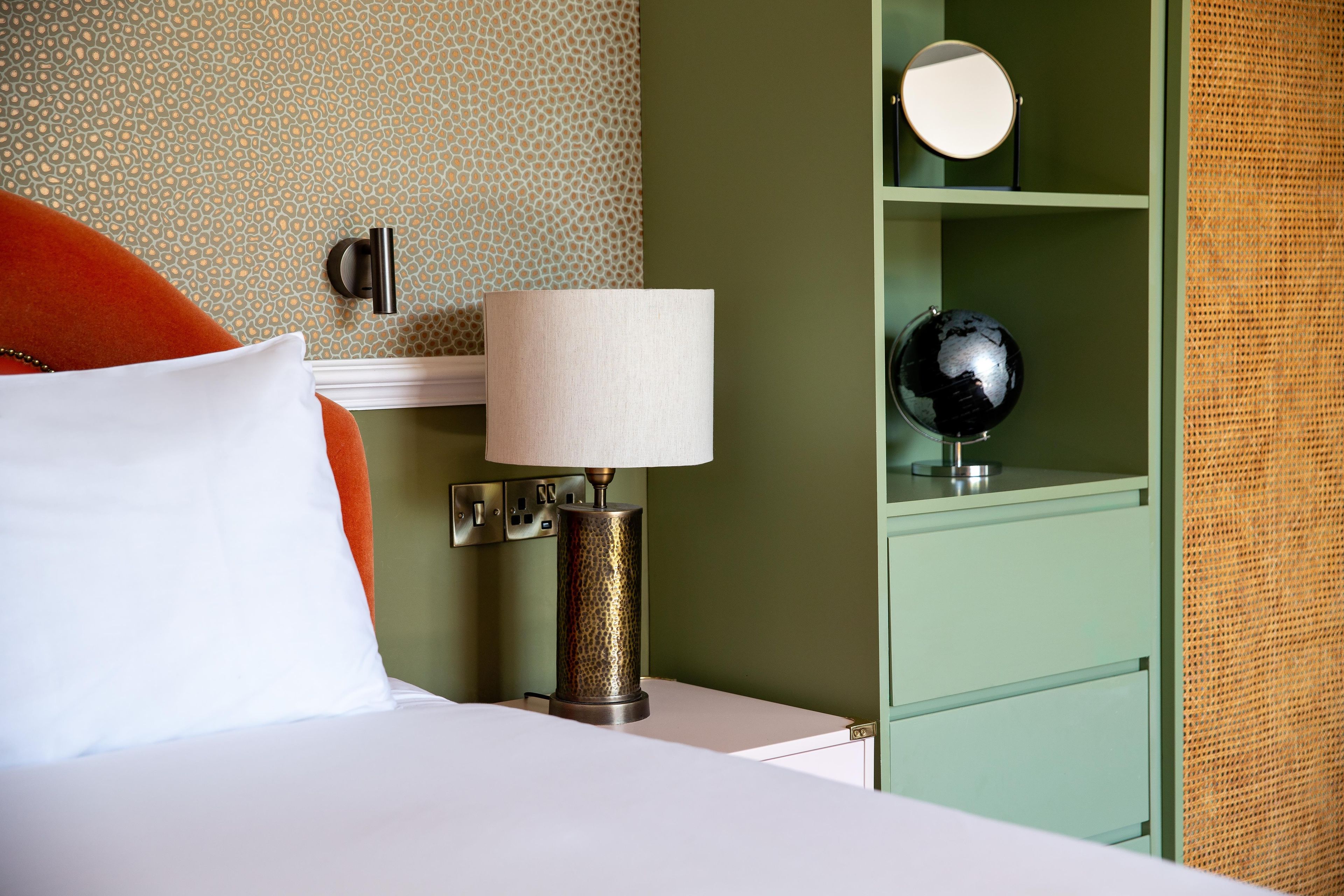 Ein Hotelzimmer mit einem Bett, einer Lampe, einem Globus und einem Spiegel auf einer Ablage.