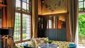 A room with a tufted sofa, two blue armchairs, a round table, and a lamp. - Elmbank York, Tapestry Collection by Hilton (York)