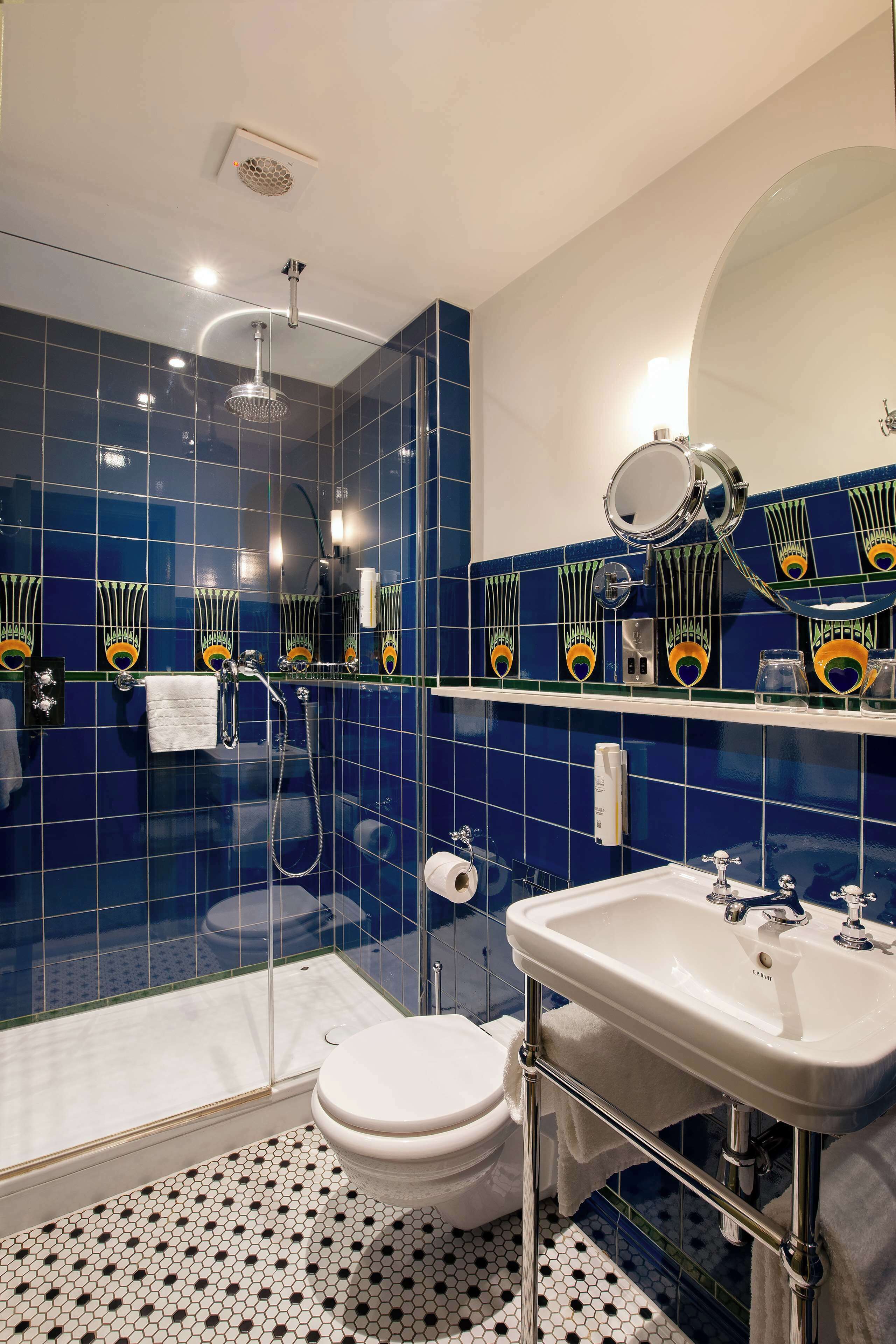 A bathroom with a glass shower enclosure, a white toilet, a sink with a mirror, and blue-tiled walls.