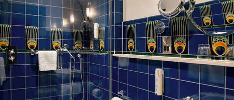 A bathroom with a glass shower enclosure, a white toilet, a sink with a mirror, and blue-tiled walls.