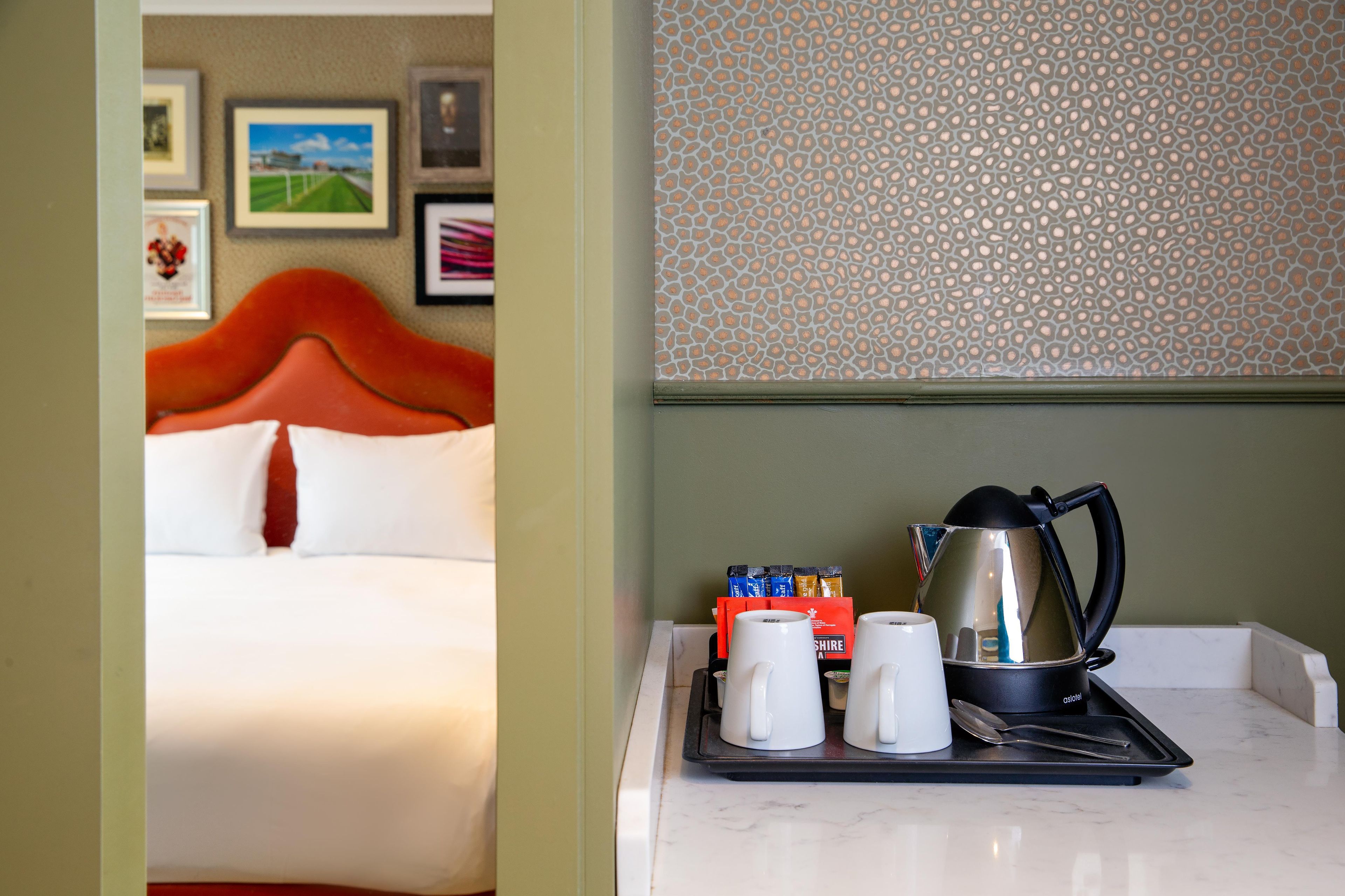 A hotel room with a bed, a tray with cups and a kettle, and a wall with a patterned design.