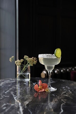 A cocktail glass with a lime slice on a marble table, accompanied by a vase with flowers and a glass of water. - Elmbank York, Tapestry Collection by Hilton (York)