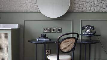 A room with a round mirror, a small table with a chair, a vintage telephone, and a wall-mounted light fixture.