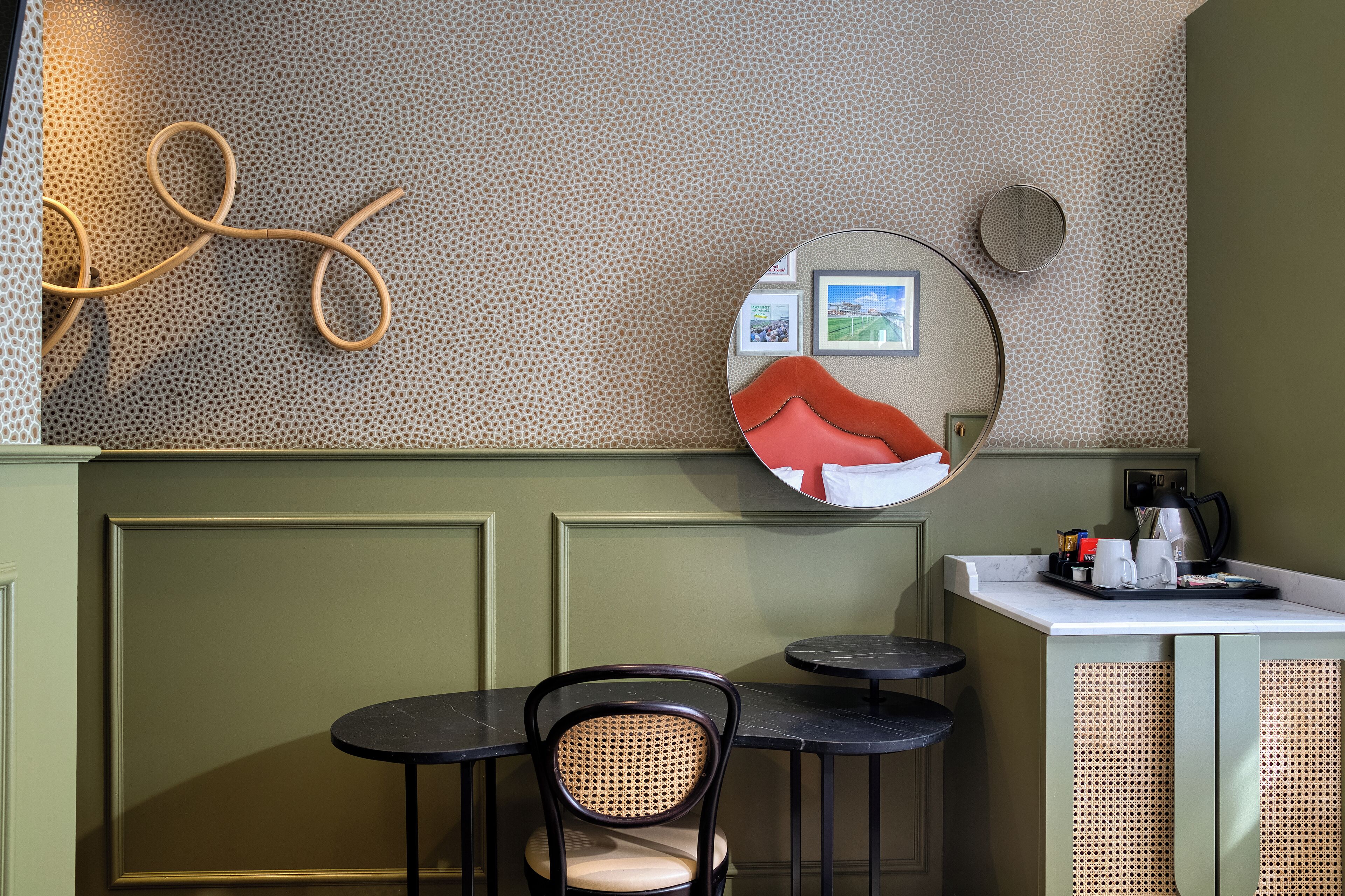 A restaurant interior with a round mirror, a wicker chair, a small round table, and a coffee station.