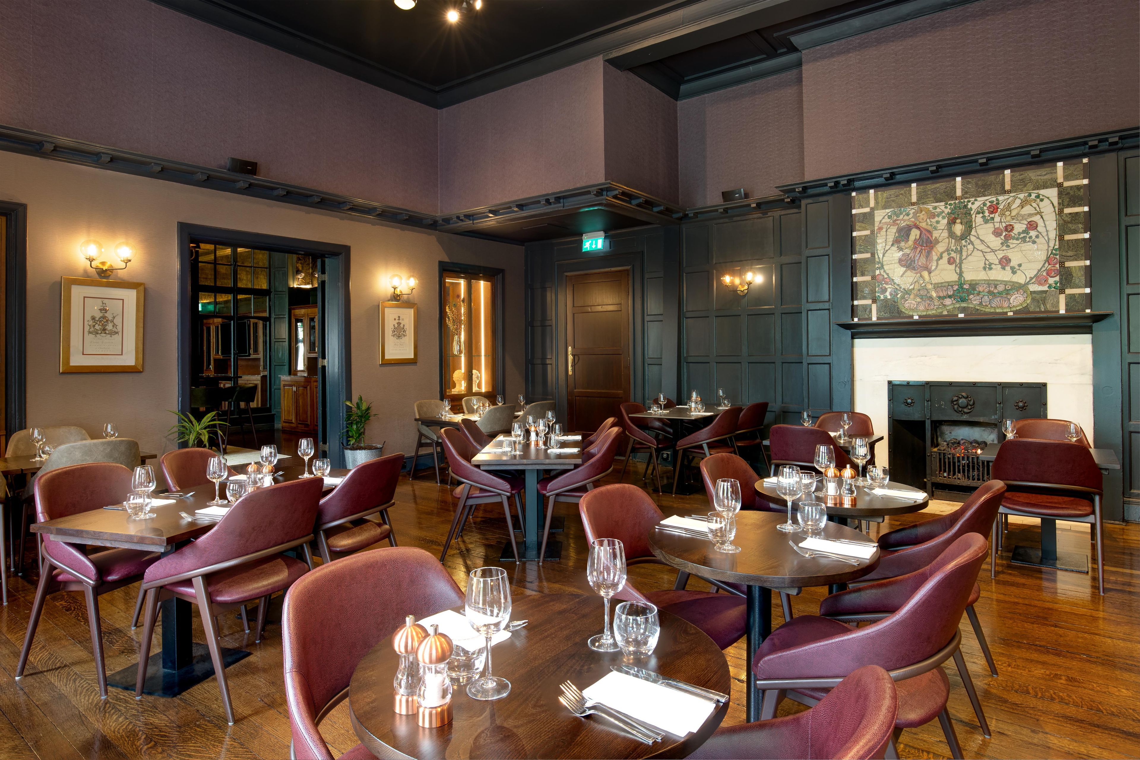 A restaurant with multiple dining tables and chairs, framed artwork on the walls, and a fireplace.