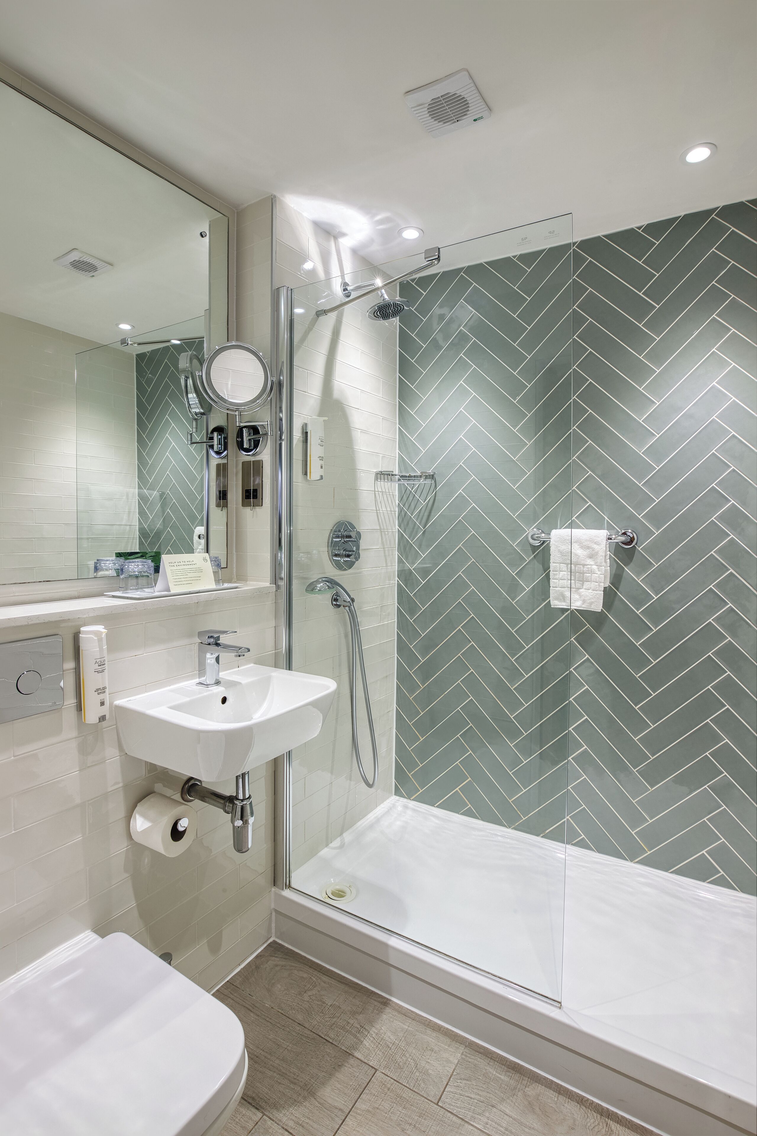 Un baño moderno con ducha separada por vidrio, lavamanos blanco y un espejo grande.