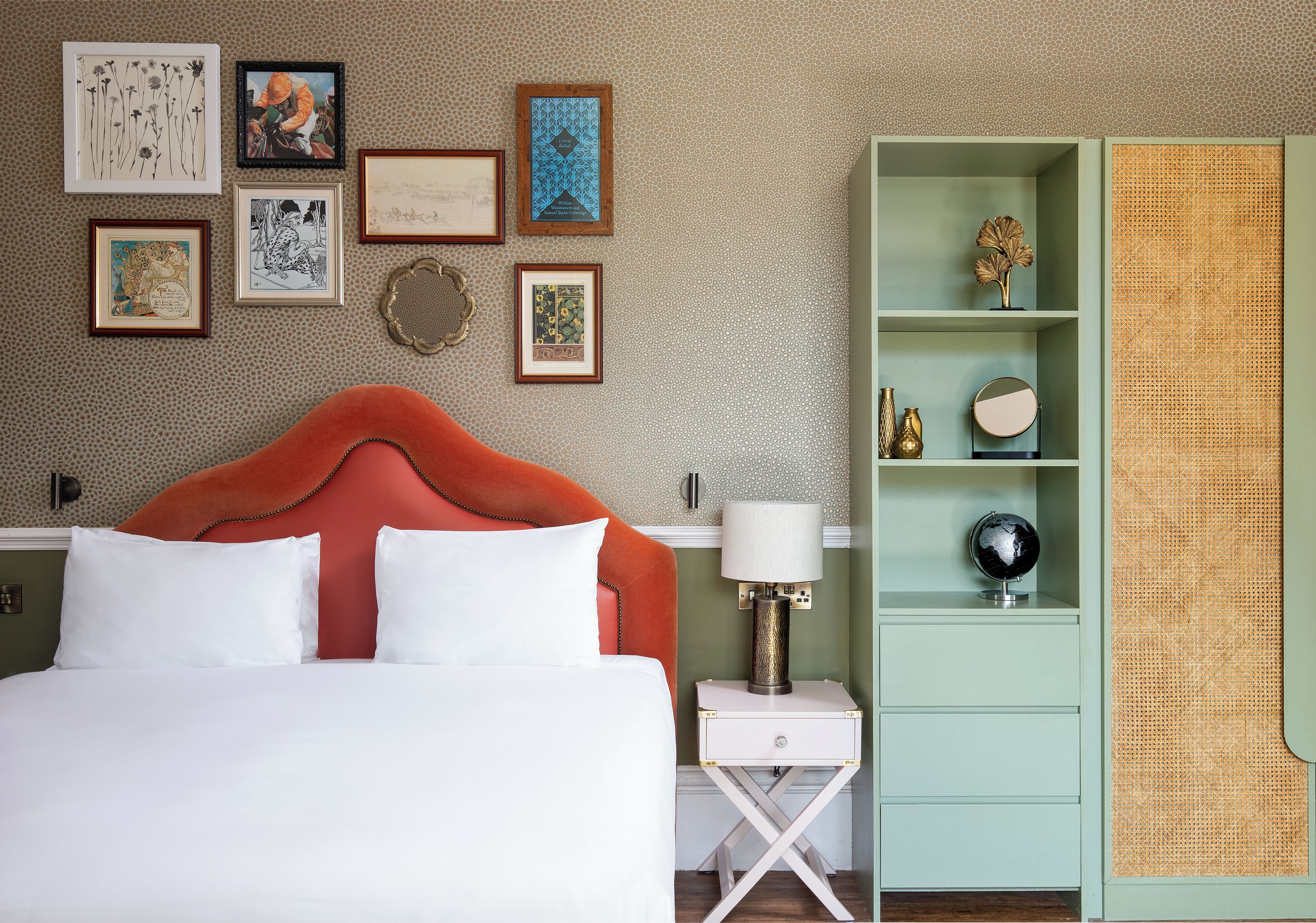Una habitación de hotel ordenada con una cama, una mesita de noche, una lámpara y un armario verde con estantes.
