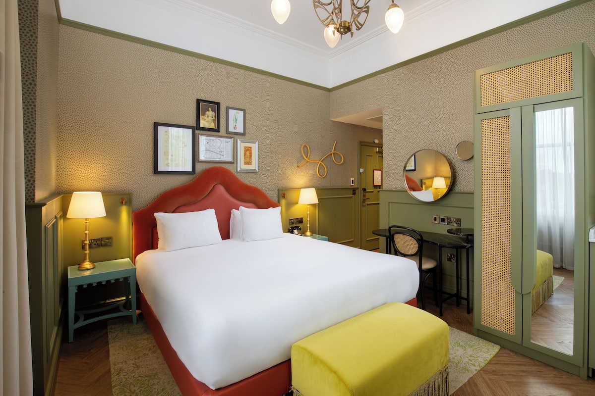 A hotel room with a large bed, bedside lamps, a desk with a chair, and a mirror.