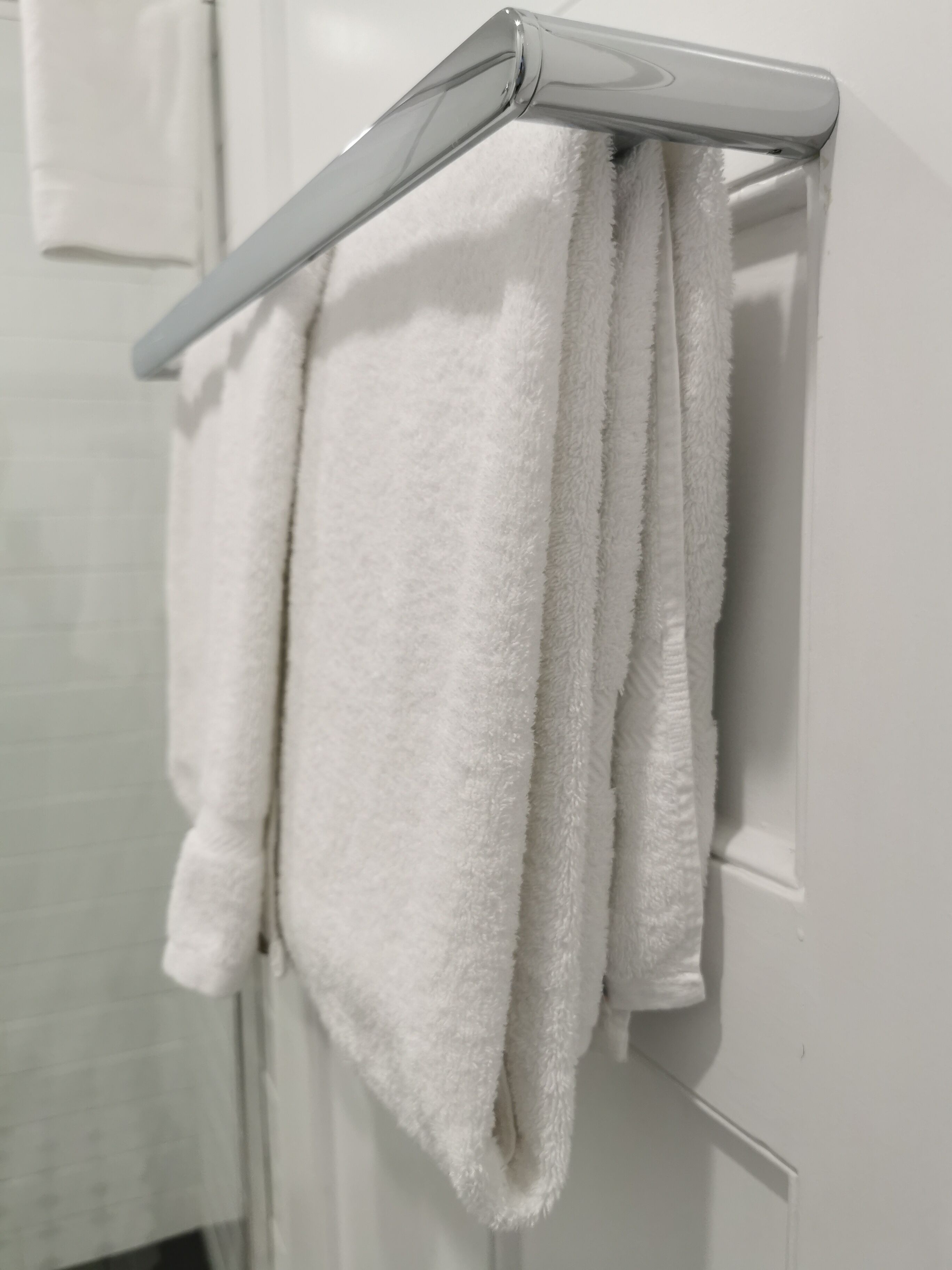 A white towel hanging on a metallic towel rack attached to a white wall.
