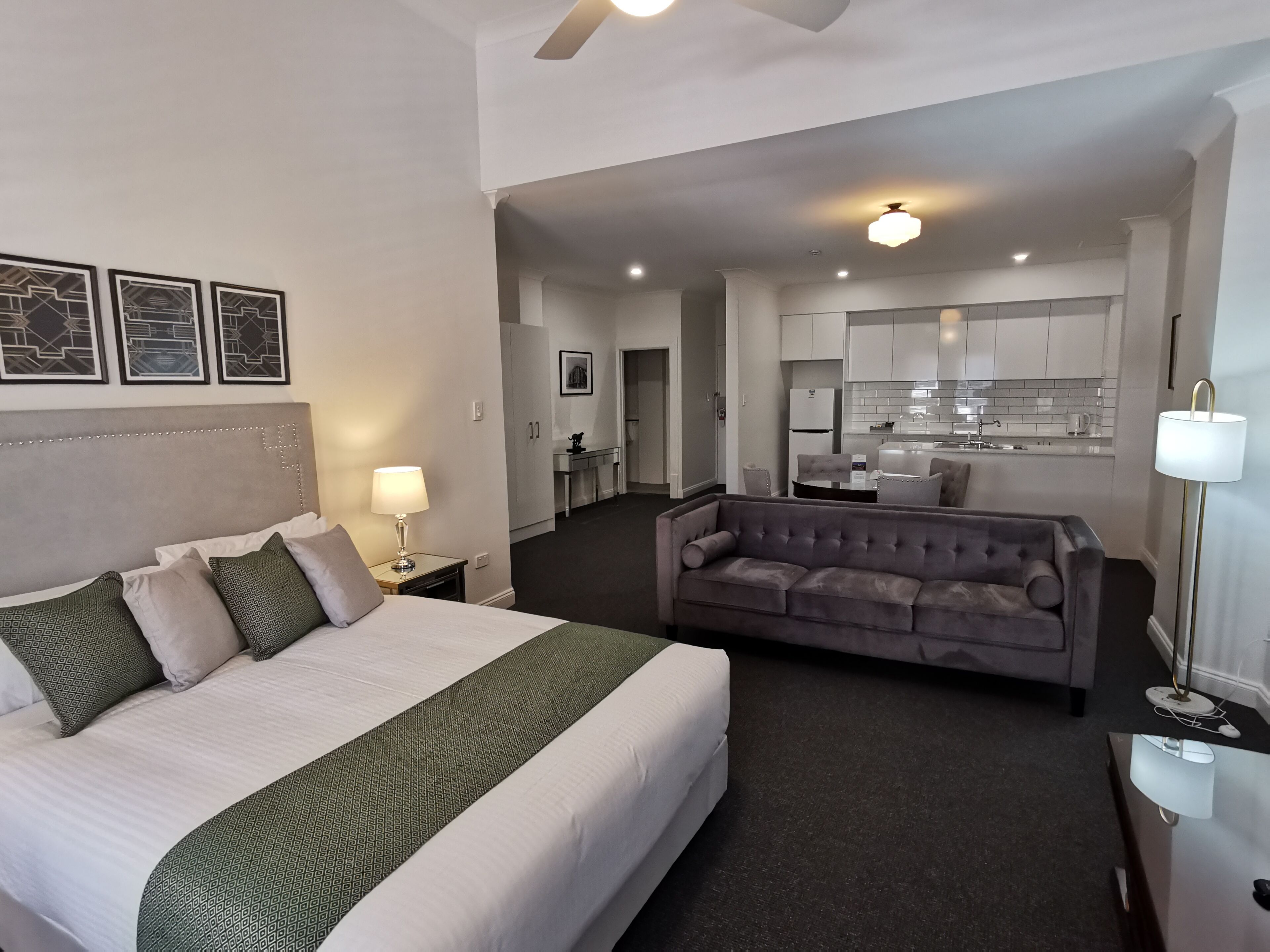 A hotel room with a bed, a sofa, a desk, and a kitchenette.