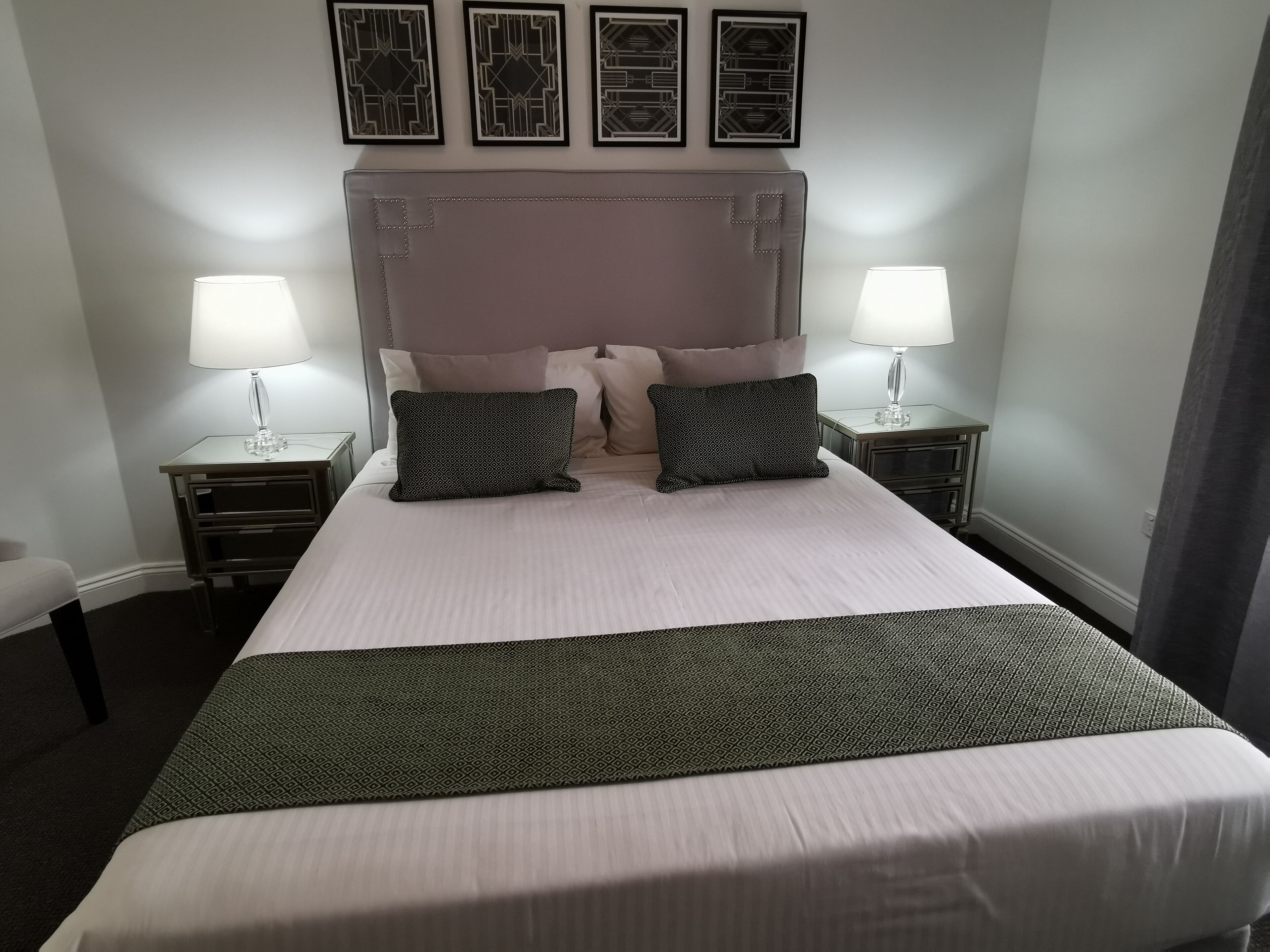 A neatly made bed with a headboard, two bedside tables with lamps, and a decorative wall piece above the bed.