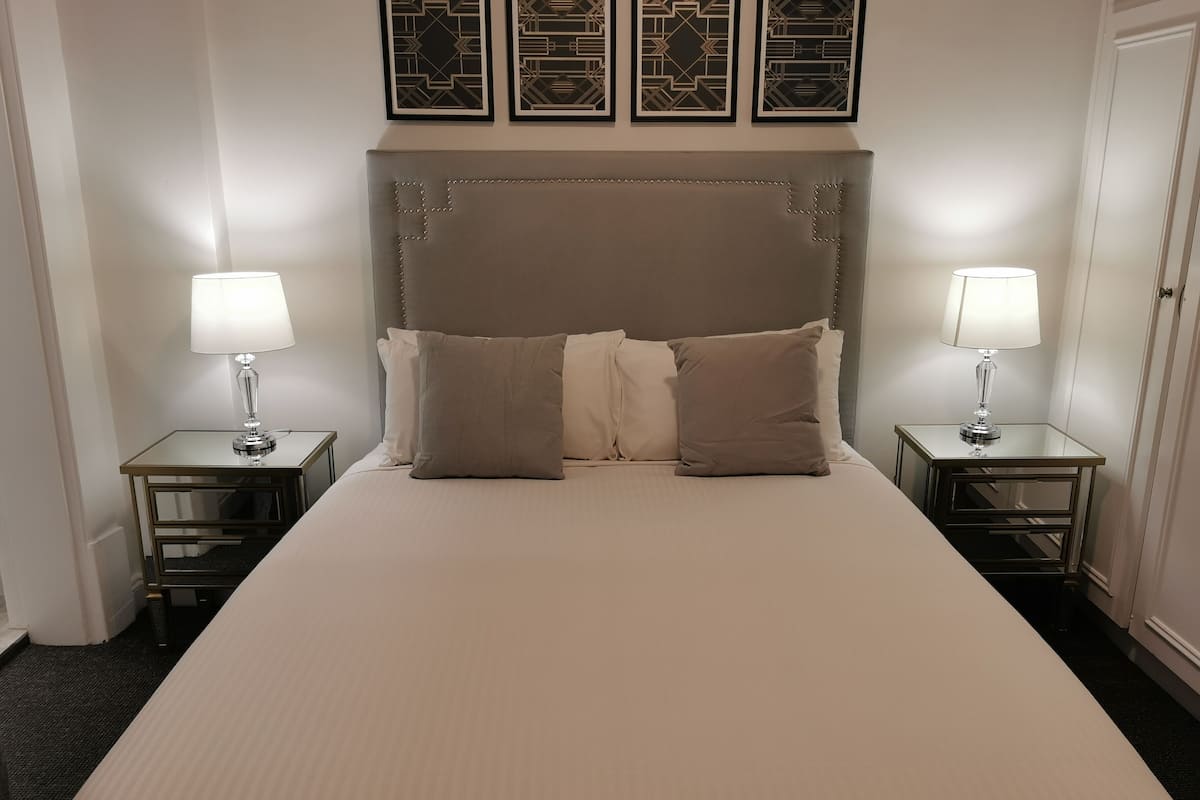 A neatly made bed with a large headboard, two bedside tables with lamps, and three framed wall decorations above the bed.