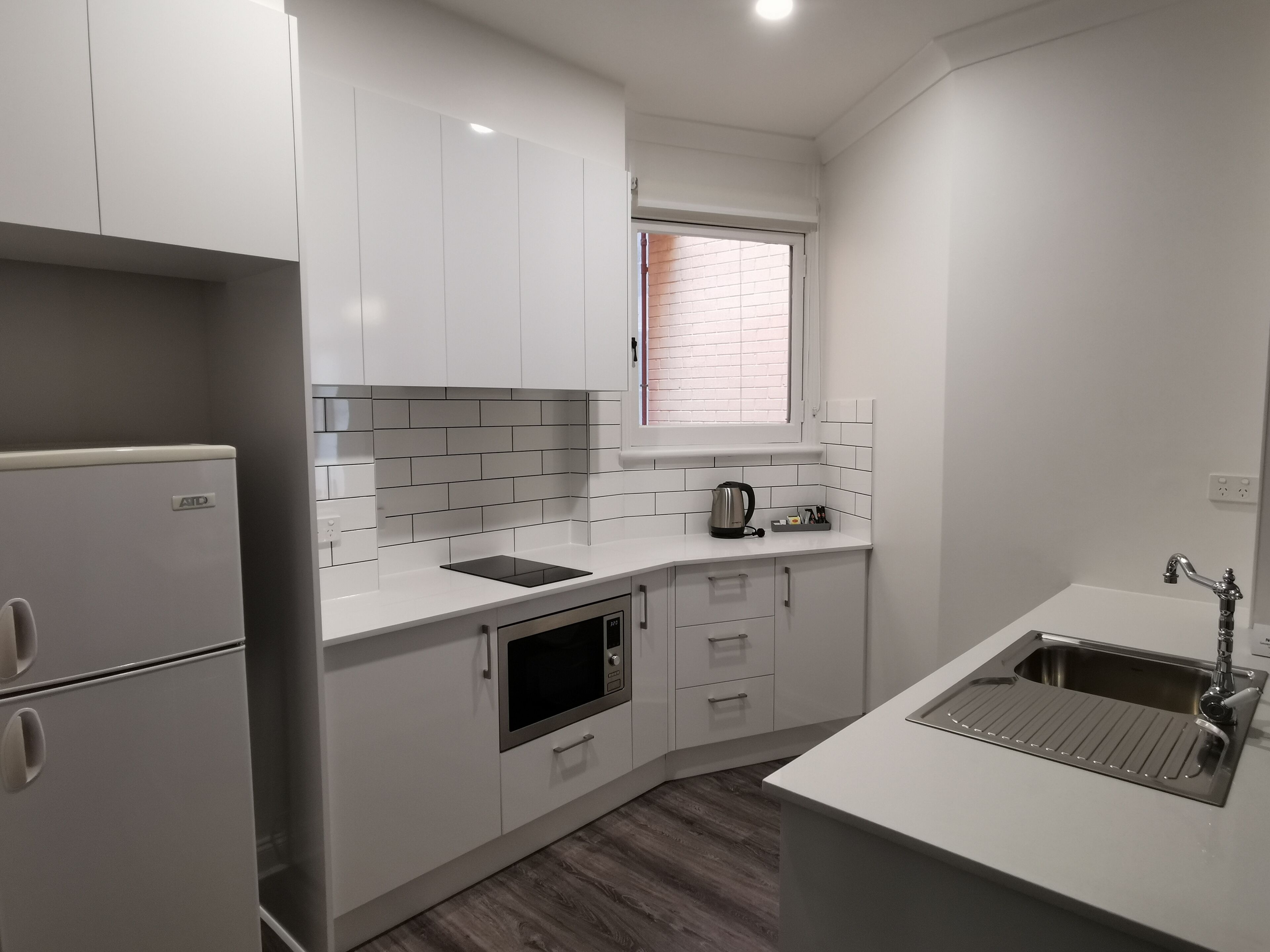 A modern kitchen with white cabinets, a built-in oven, a window, and a stainless steel sink.