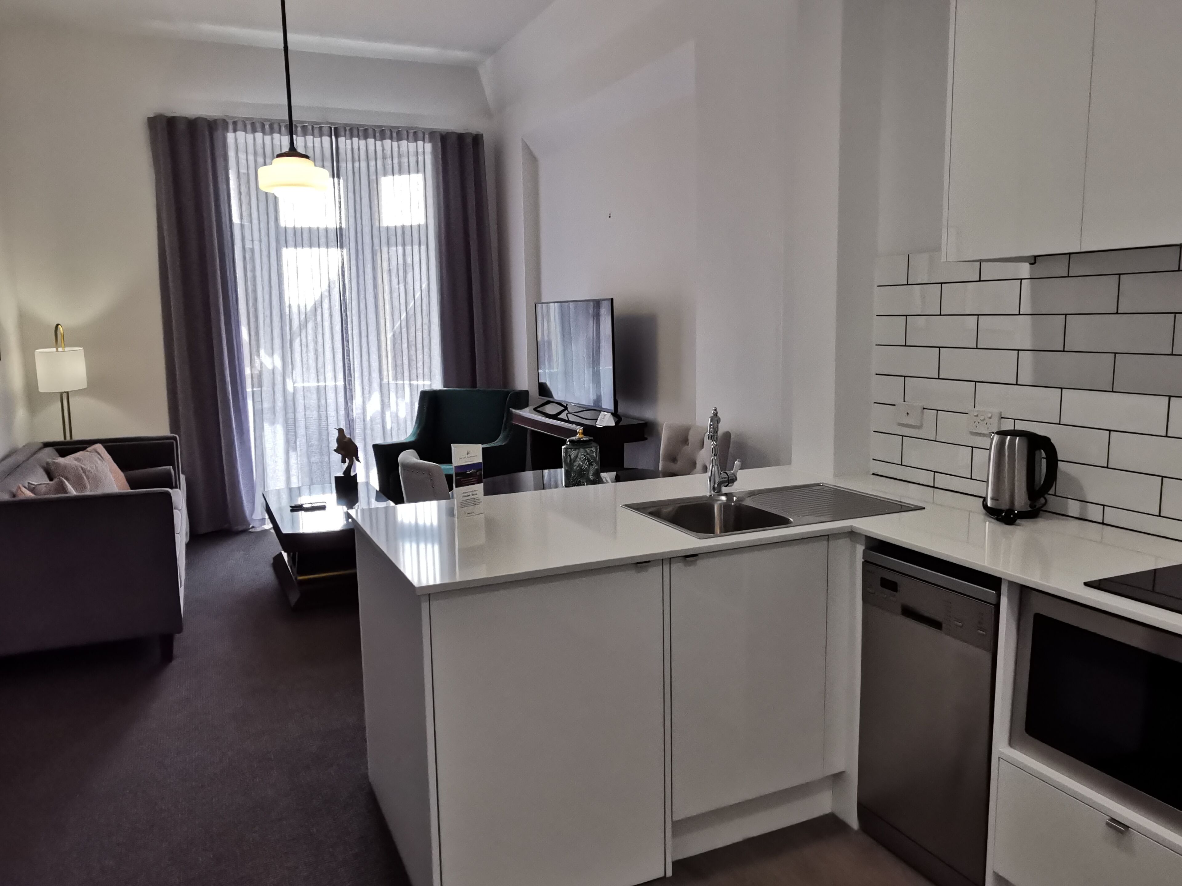 A compact hotel room with a kitchenette, a sofa, a dining table, and a TV.