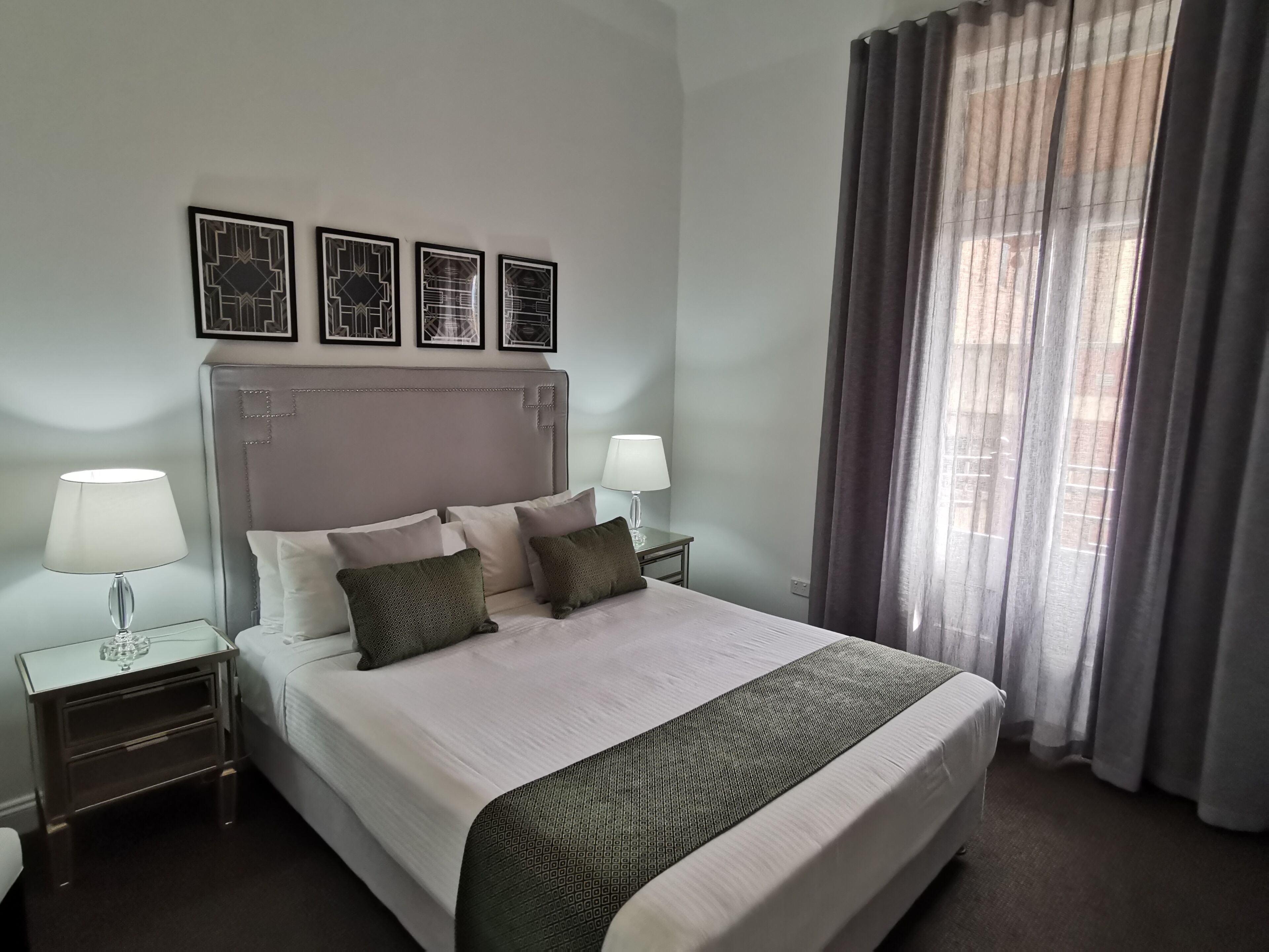 A neatly made bed with a patterned throw, two bedside lamps, and a headboard with a decorative panel.