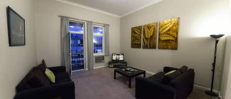 Una sala de estar con dos sofás negros, una mesa de centro, un televisor y obras de arte en la pared.