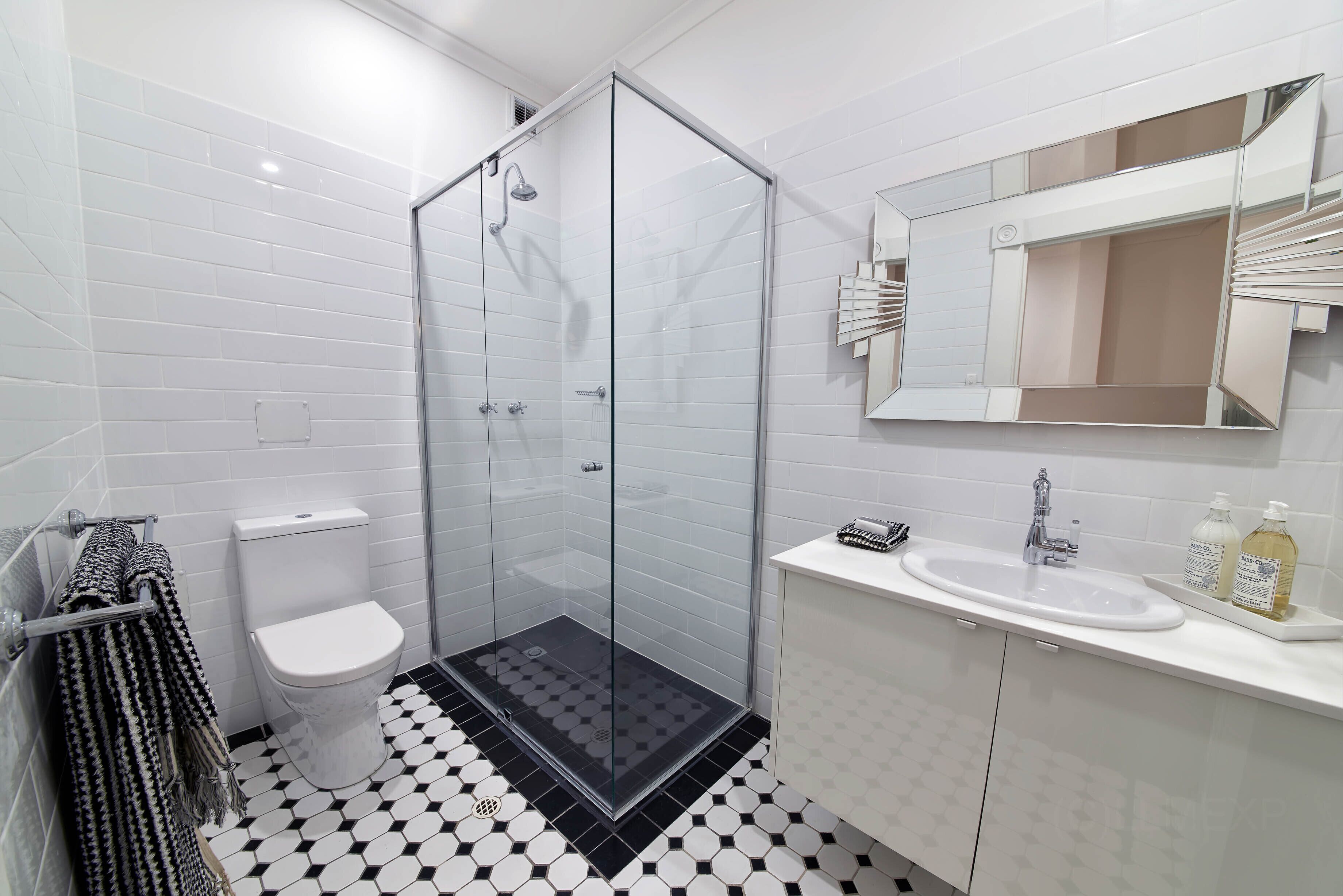 A modern bathroom with a glass-enclosed shower, a white toilet, and a sink with a mirror above it.