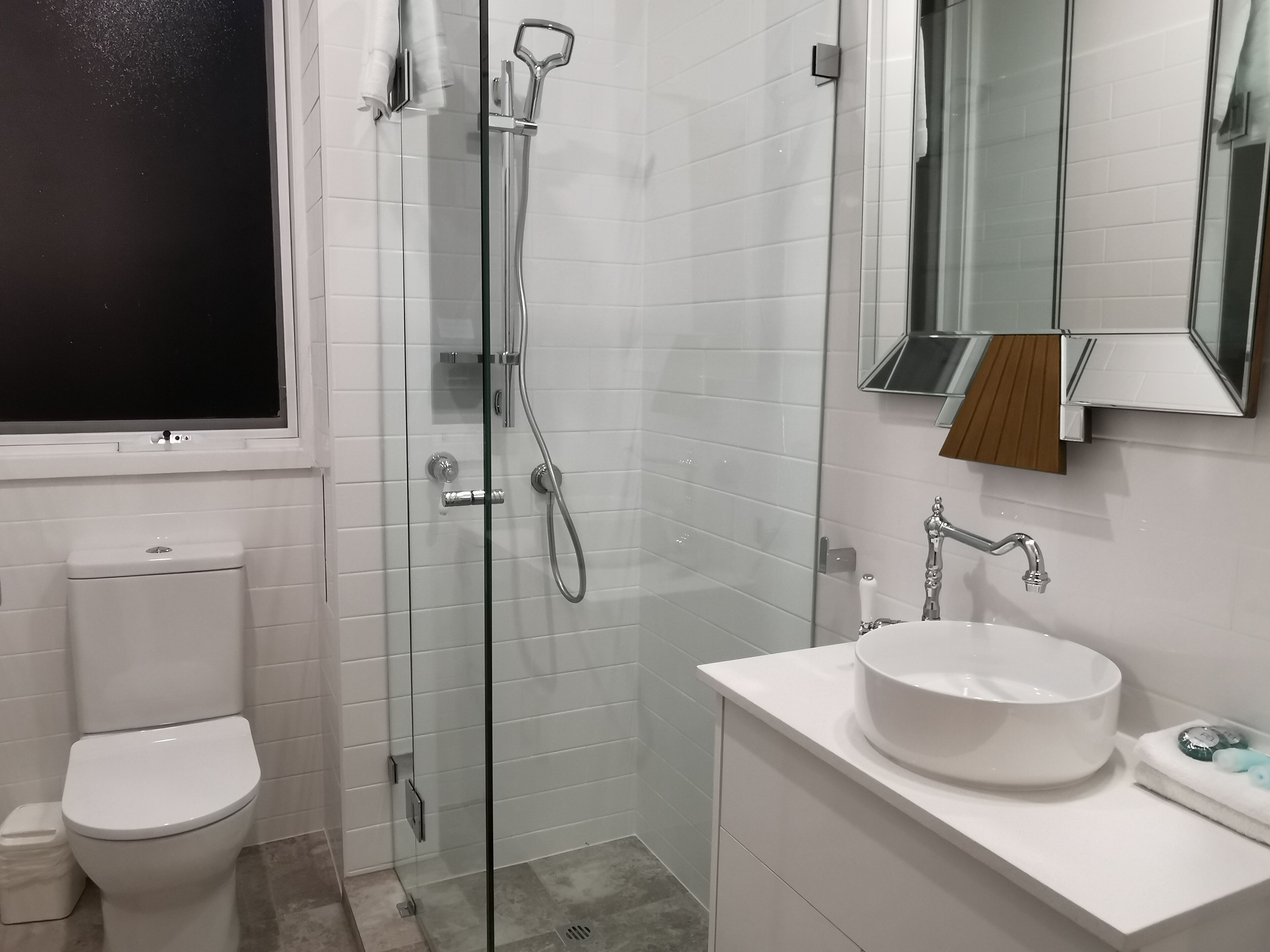 Un baño moderno con ducha envuelta en vidrio, un inodoro blanco y un lavamanos con espejo.