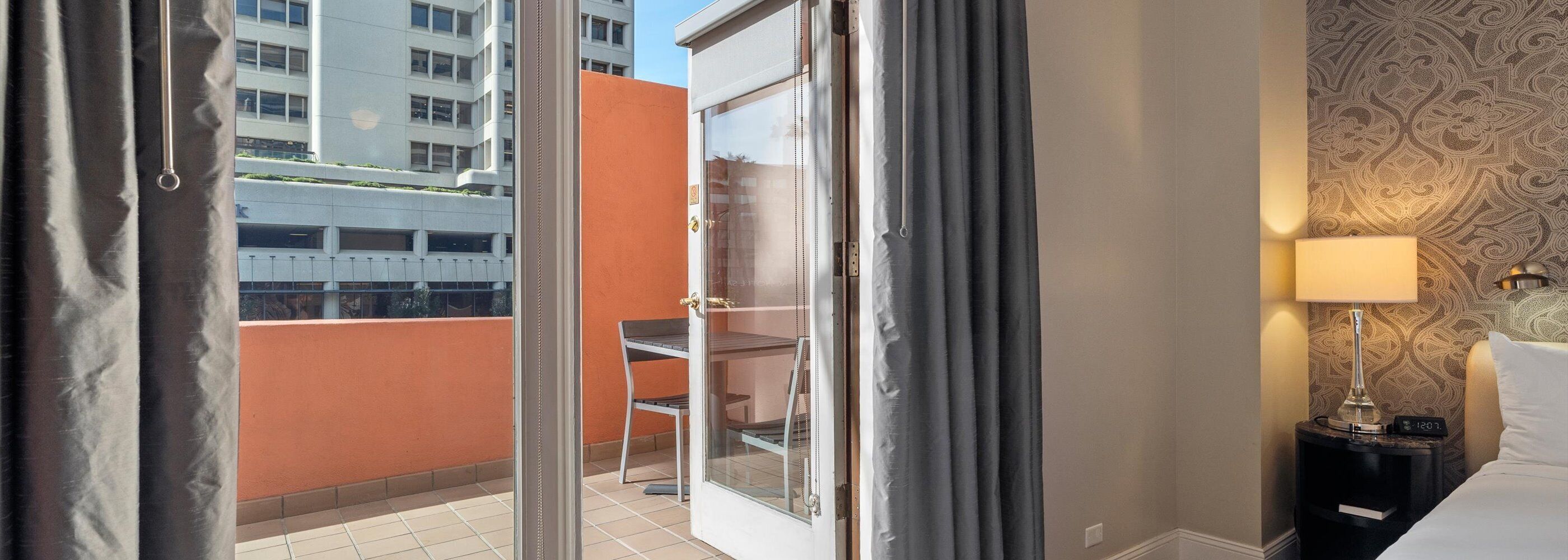 Ein Hotelzimmer mit einer Schiebetür zum Balkon, einem kleinen Tisch mit einem Stuhl, einer Lampe und einer Wand mit Musterpapier.