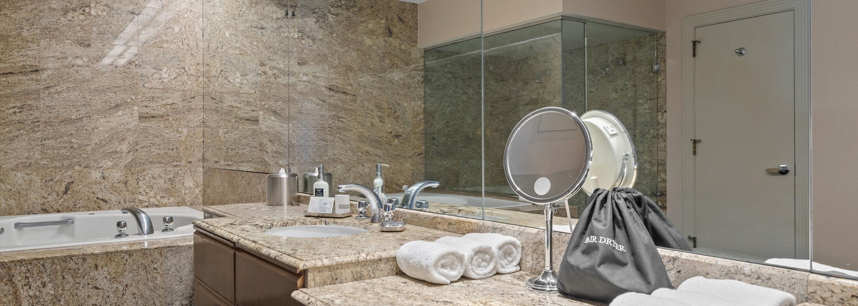 Un baño con encimera de mármol, lavamanos, espejo, toallero y cabina de ducha de vidrio.