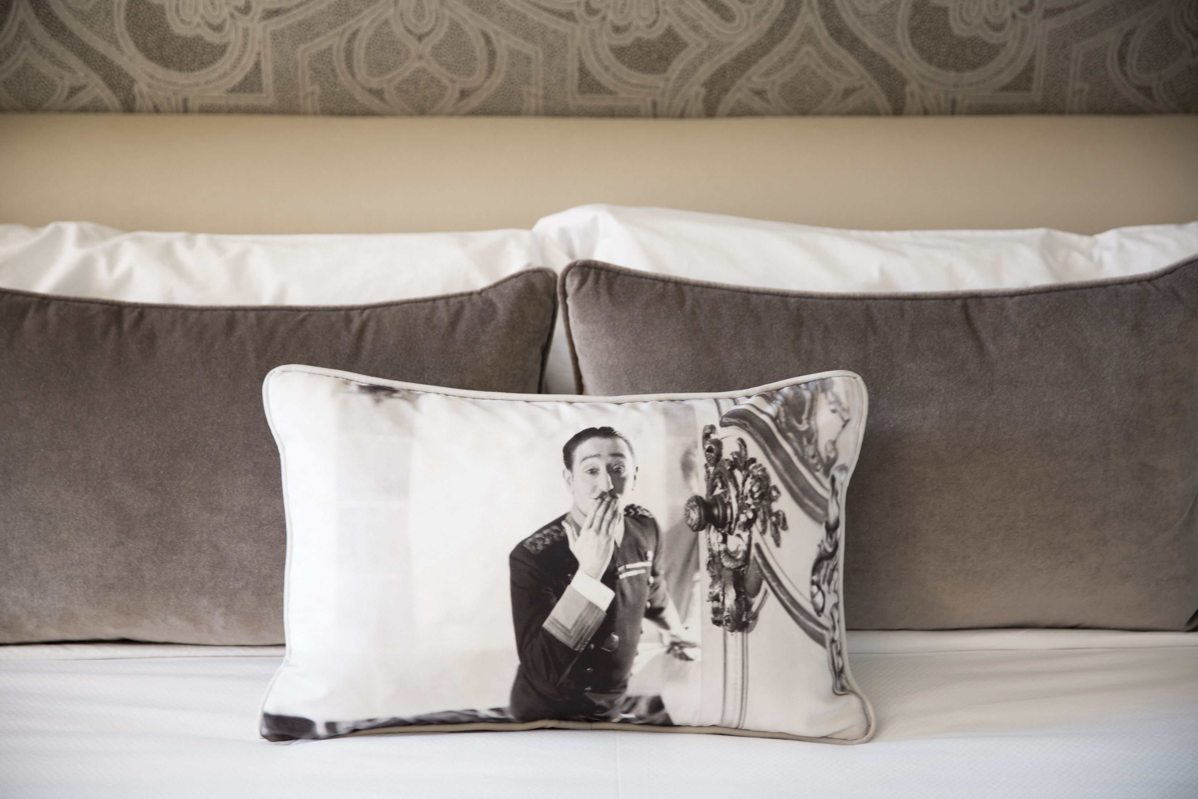 A pillow with a black and white photo of a person in uniform, placed on a bed with two pillows behind it.