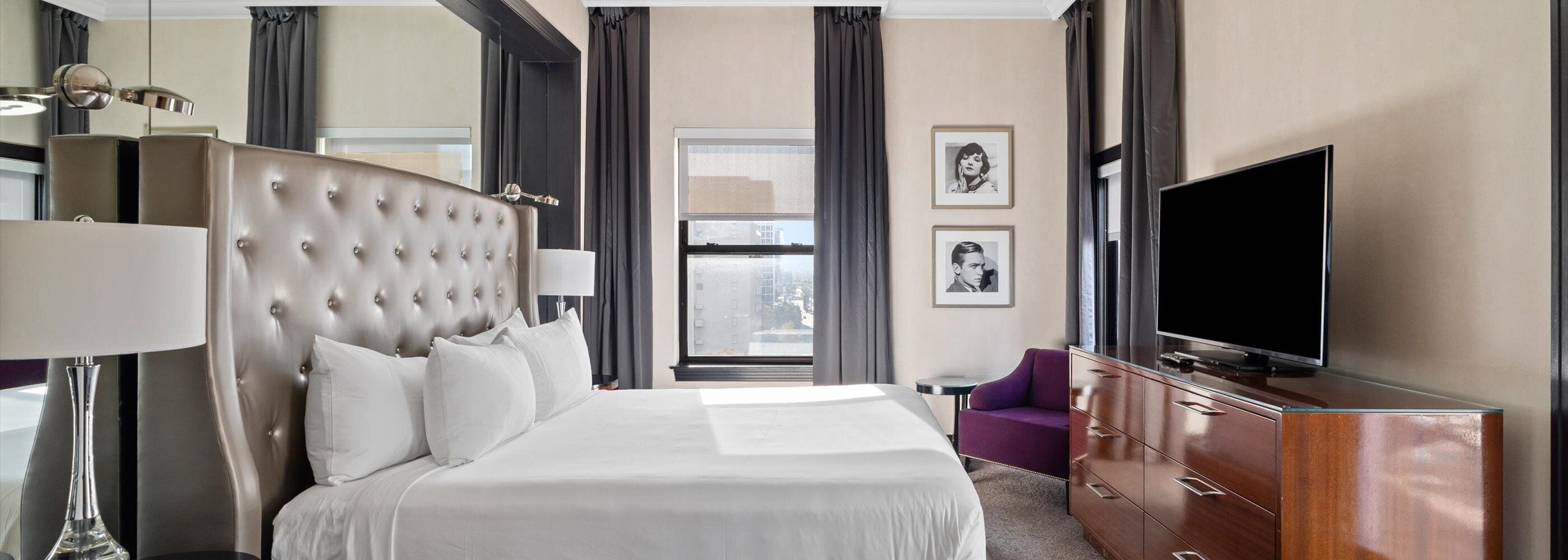 A hotel room with a large bed, a flat-screen TV, a dresser, and a window with curtains.