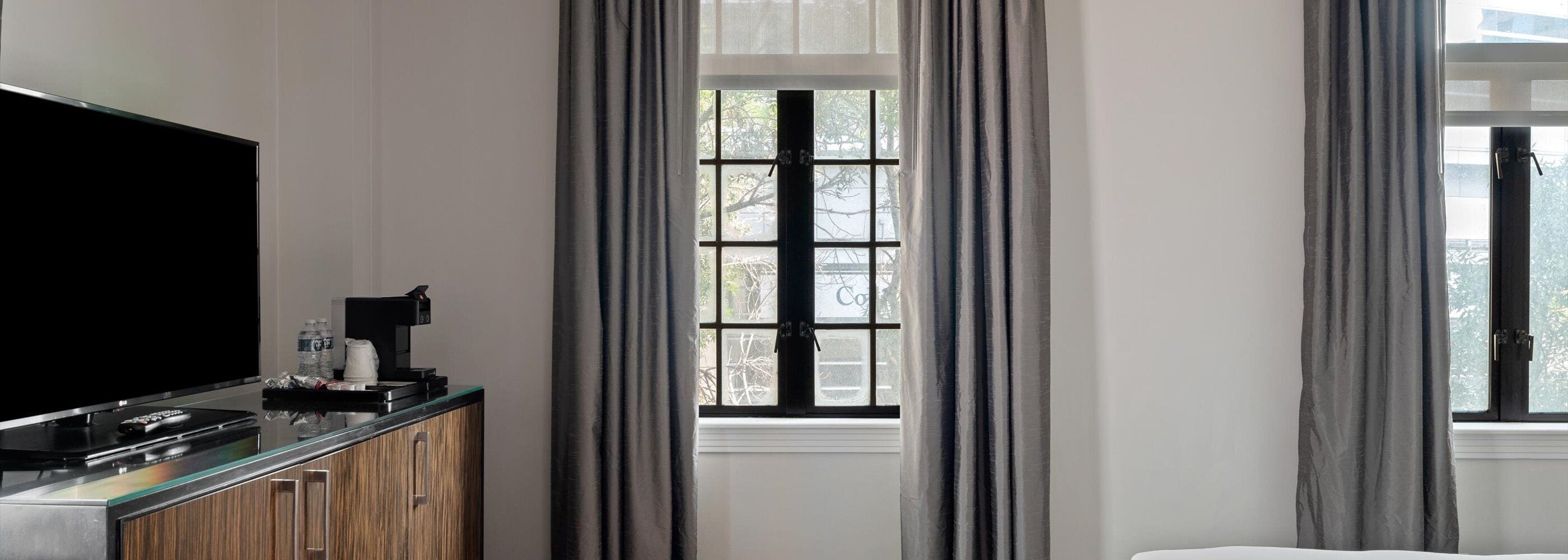 Quarto de hotel com televisão de tela plana, cafeteira e janela com cortinas.