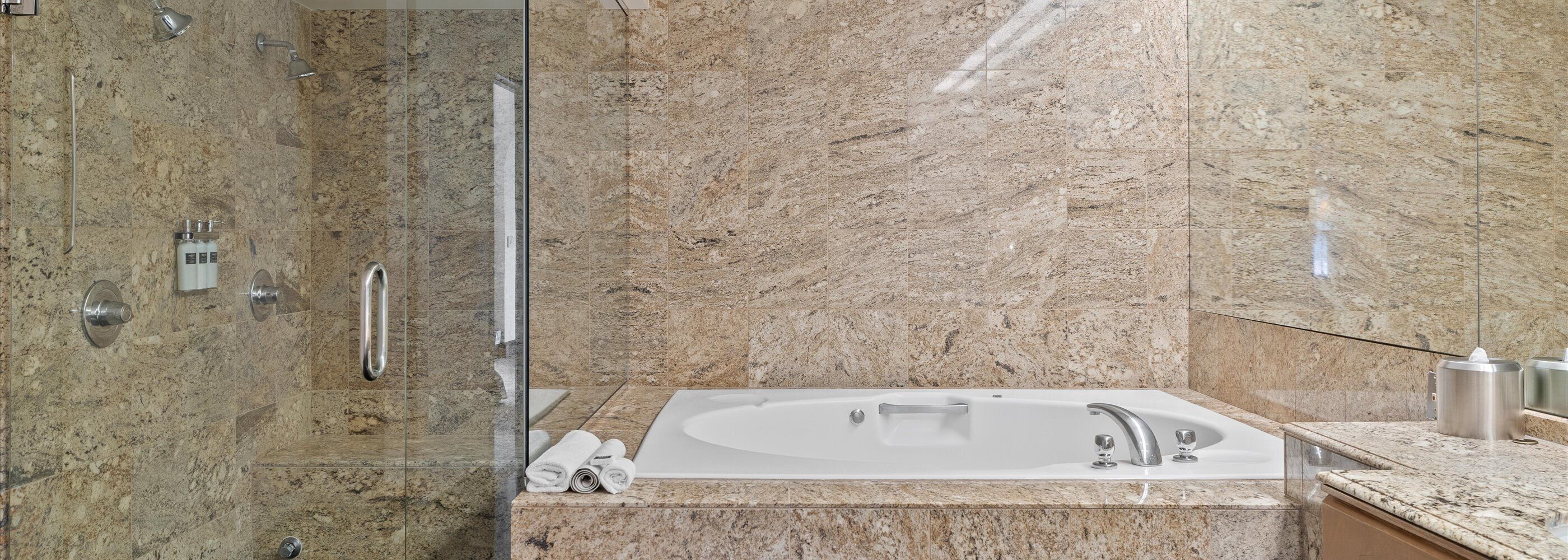 Une salle de bain moderne dotée d’une douche à parois de verre, d’une baignoire sur pieds et d’un mur recouvert de carreaux de marbre.