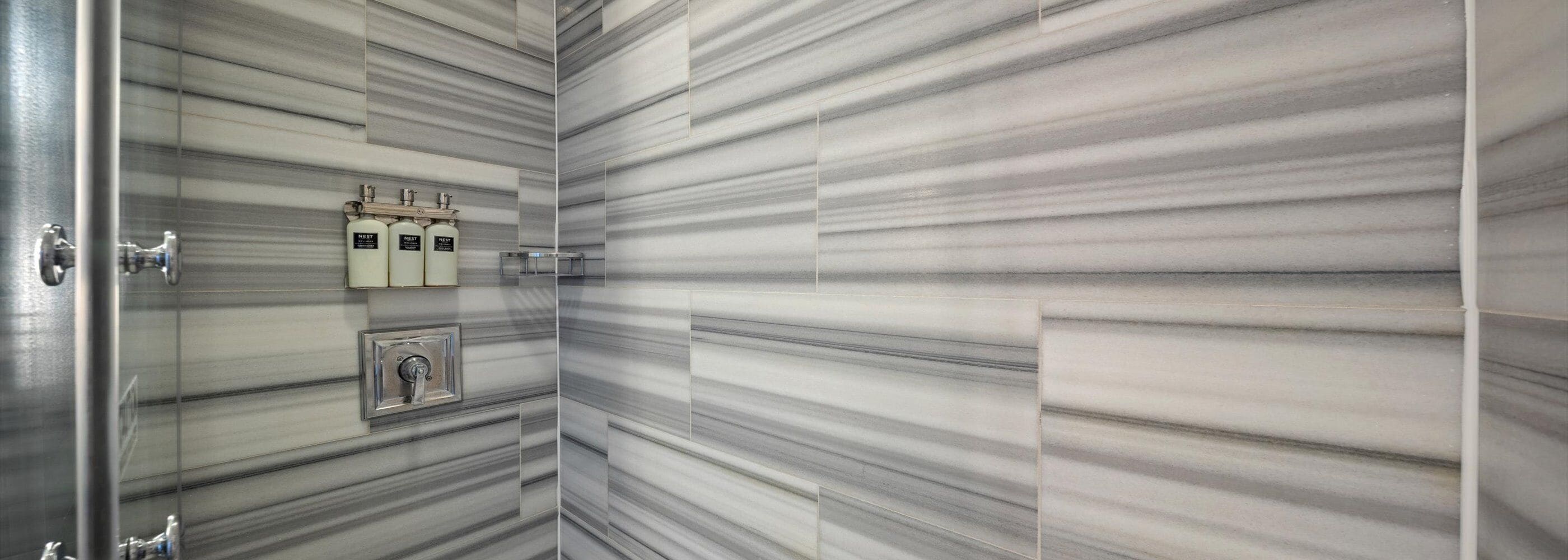 A bathroom with a marble wall and a towel rack with three bottles.