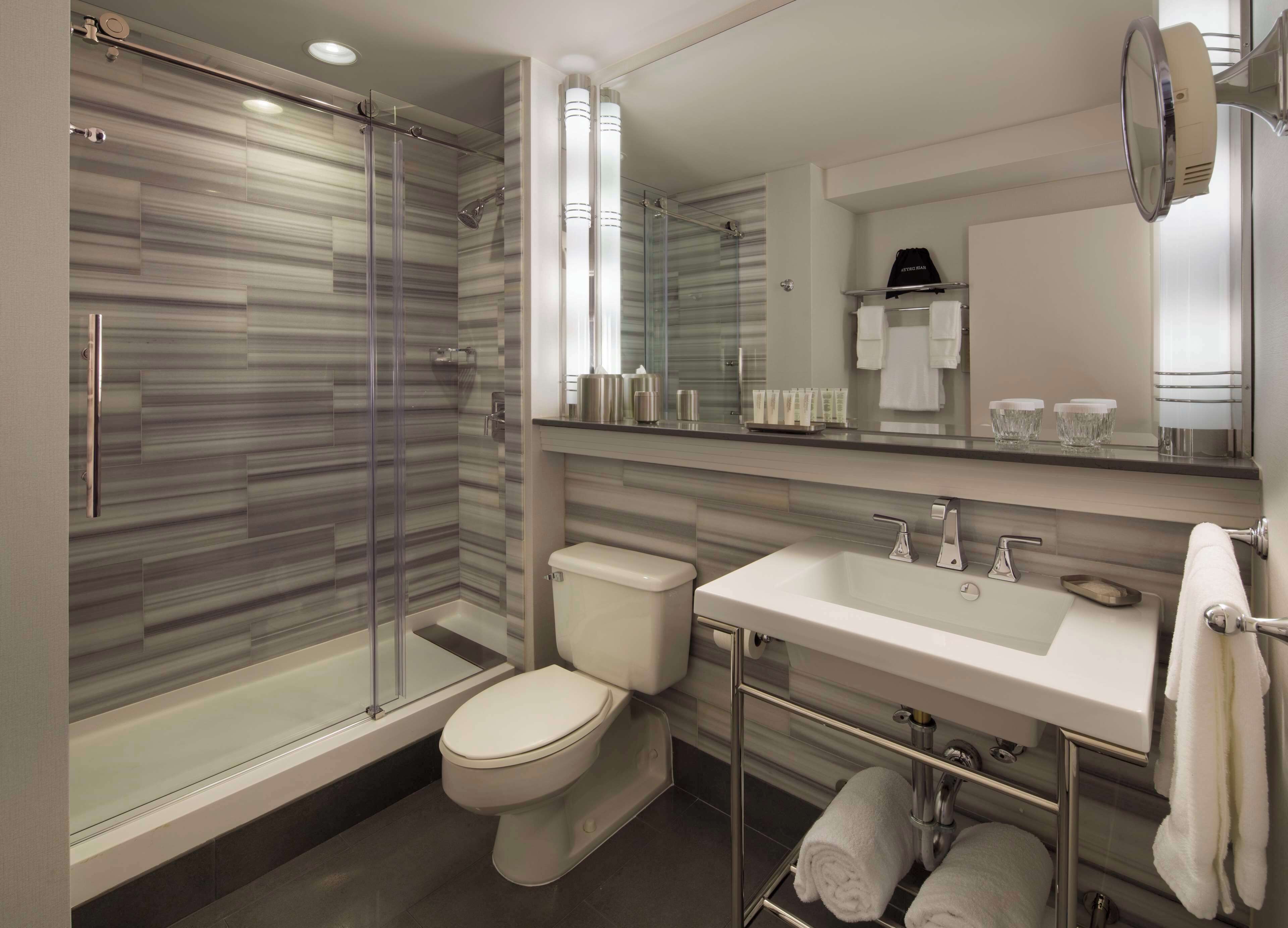 A modern bathroom with a glass-enclosed shower, a white toilet, a large mirror, and a vanity with a sink and towel rack.