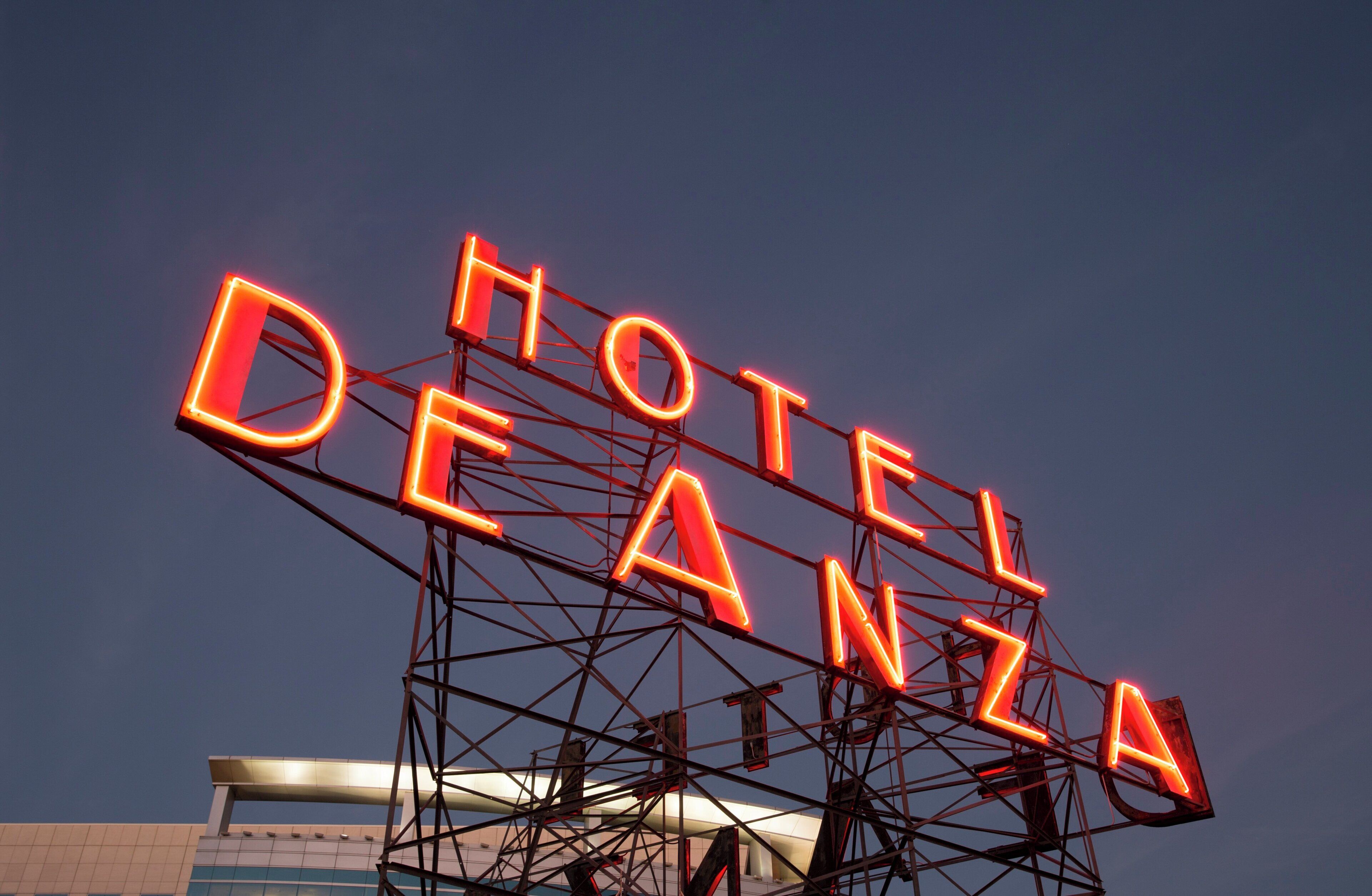 Une enseigne au néon qui affiche le mot « HÔTEL DEANZA » sur un ciel crépusculaire.
