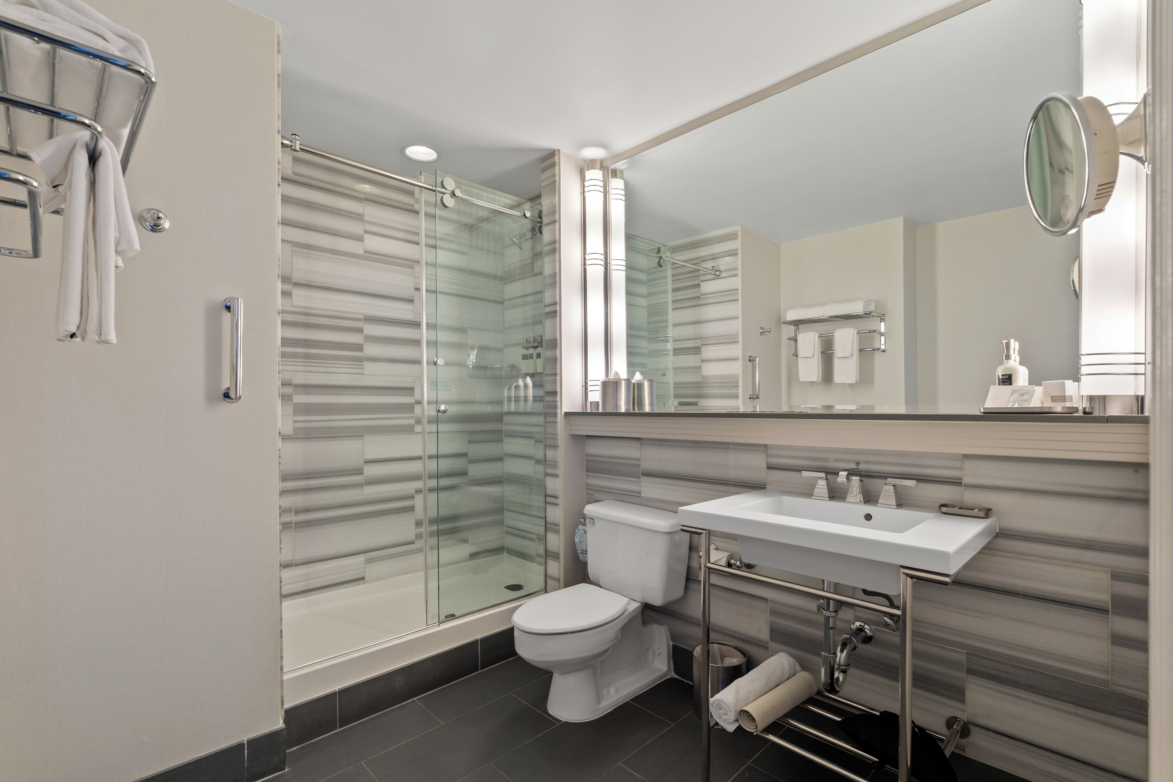 A modern bathroom with a glass-enclosed shower, a toilet, a sink, and a large mirror.