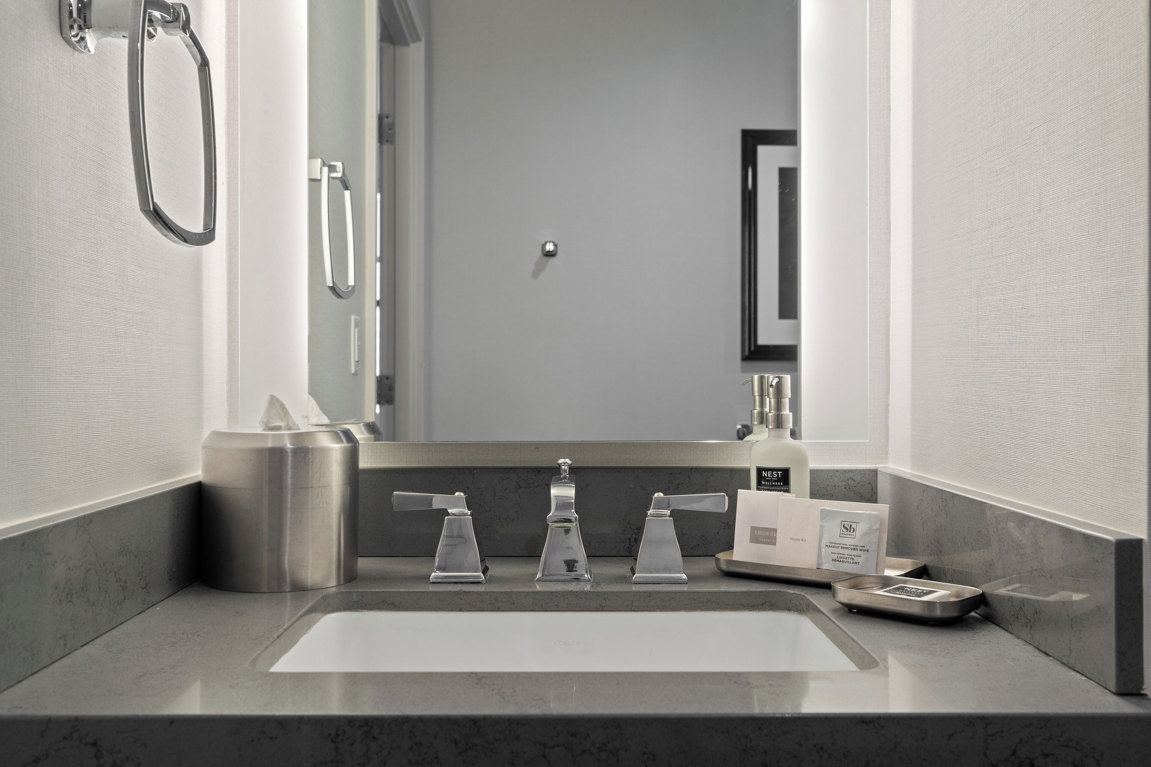 A modern bathroom with a large mirror, a sink with three faucets, and a shower area.