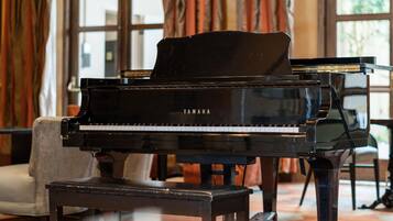Un pianoforte a coda in una stanza luminosa, con ampie finestre, un divano e un tavolo.