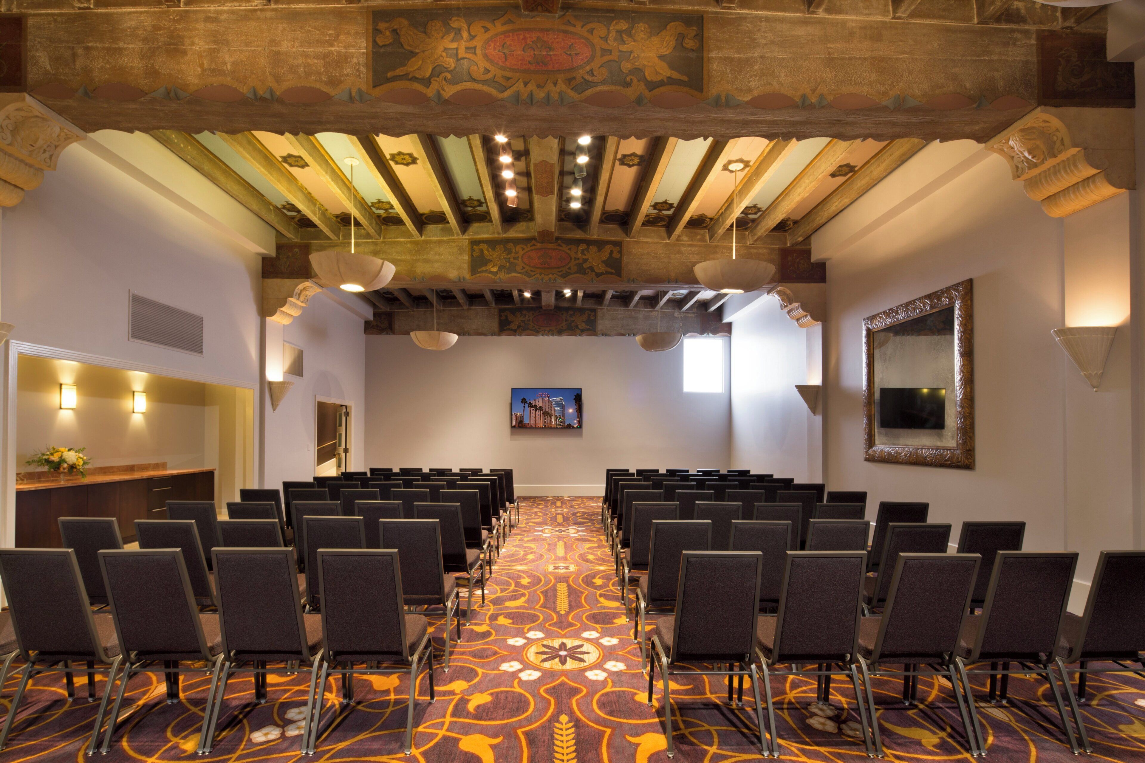Un salón de conferencias con filas de sillas, una alfombra estampada y un techo alto con detalles decorativos.