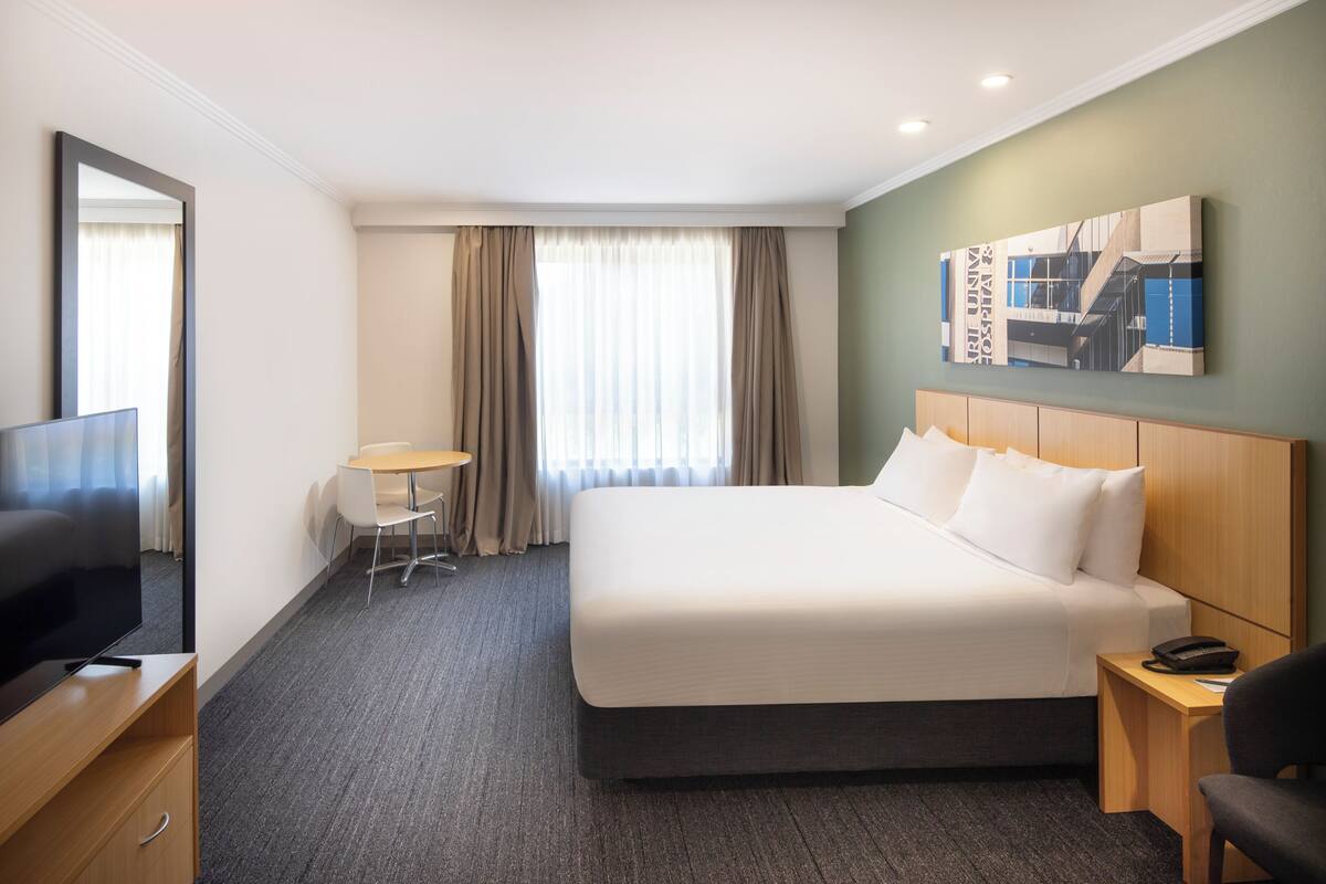 Ein Hotelzimmer mit einem großen Bett, einem Schreibtisch mit Stuhl, einem Fernseher und einem Gemälde an der Wand.