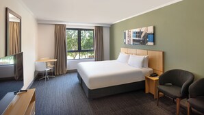 A hotel room with a large bed, a desk, a chair, and a window with curtains.