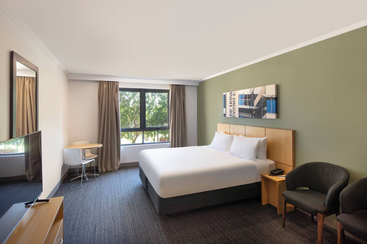 Ein Hotelzimmer mit einem großen Bett, einem Schreibtisch, einem Stuhl und einem Fenster mit Vorhängen.