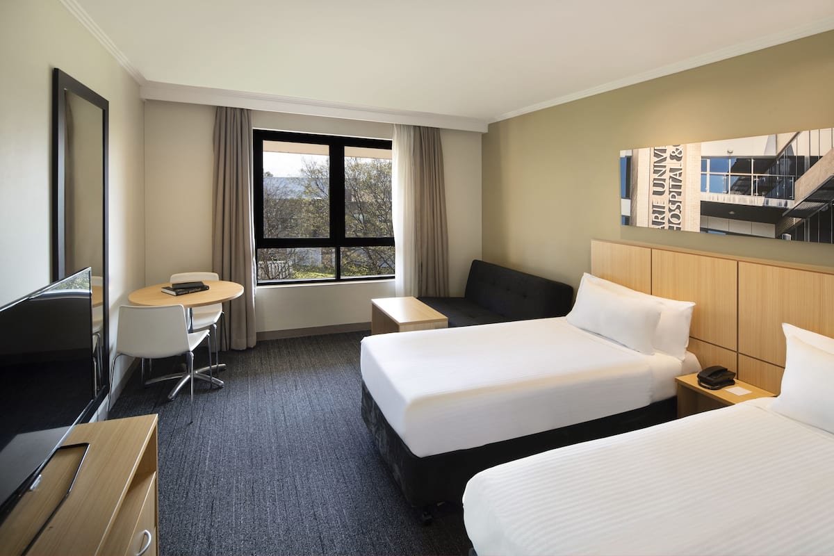 Ein Hotelzimmer mit zwei Betten, einem Schreibtisch, einem Stuhl, einem Fernseher und einem Fenster mit Vorhängen.