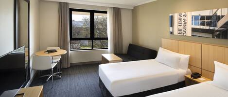 Habitación de hotel con dos camas, un escritorio, una silla, un televisor y una ventana con cortinas.
