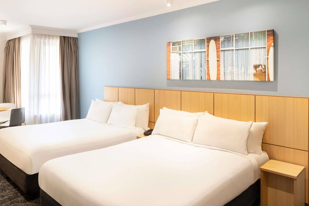 A hotel room with two beds, a desk, and a large window with curtains.