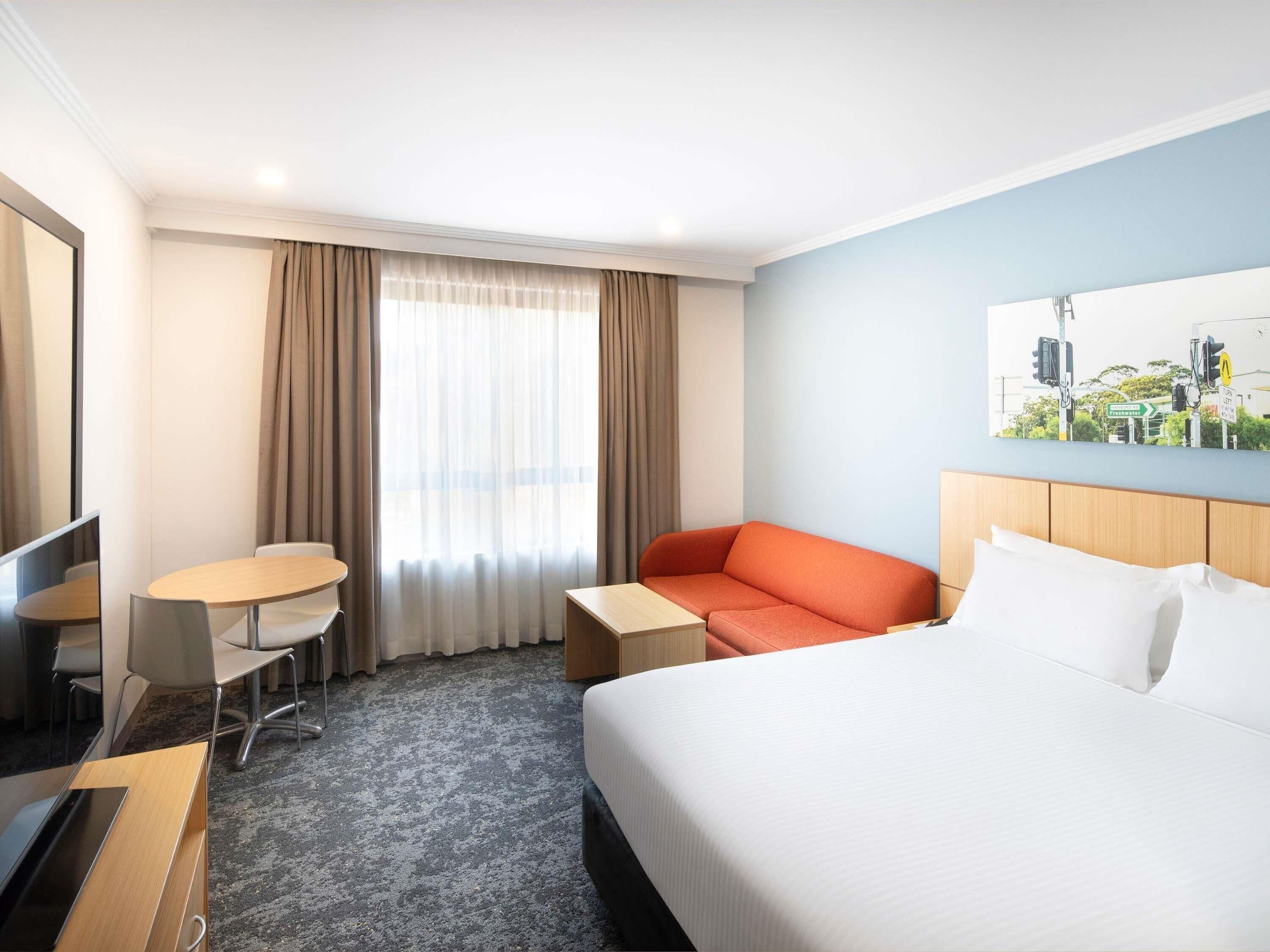 Habitació d'hotel amb un llit, escriptori, cadira, sofà i finestra amb cortines.
