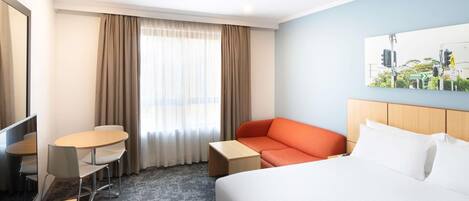 Habitació d'hotel amb un llit, escriptori, cadira, sofà i finestra amb cortines.
