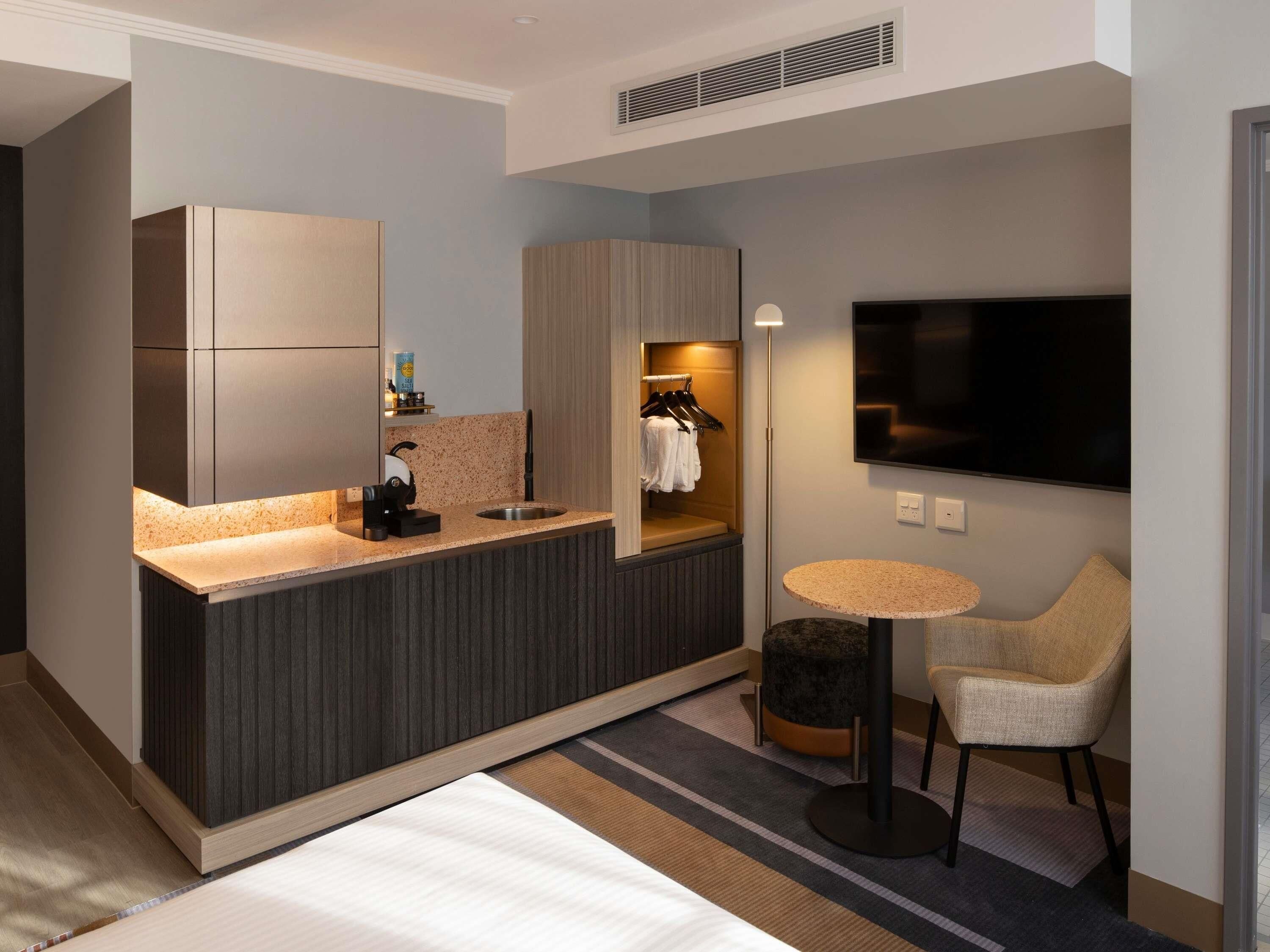 Ett modernt hotellrum med ett litet kök, en platt-TV, ett runt bord och en sittgrupp.